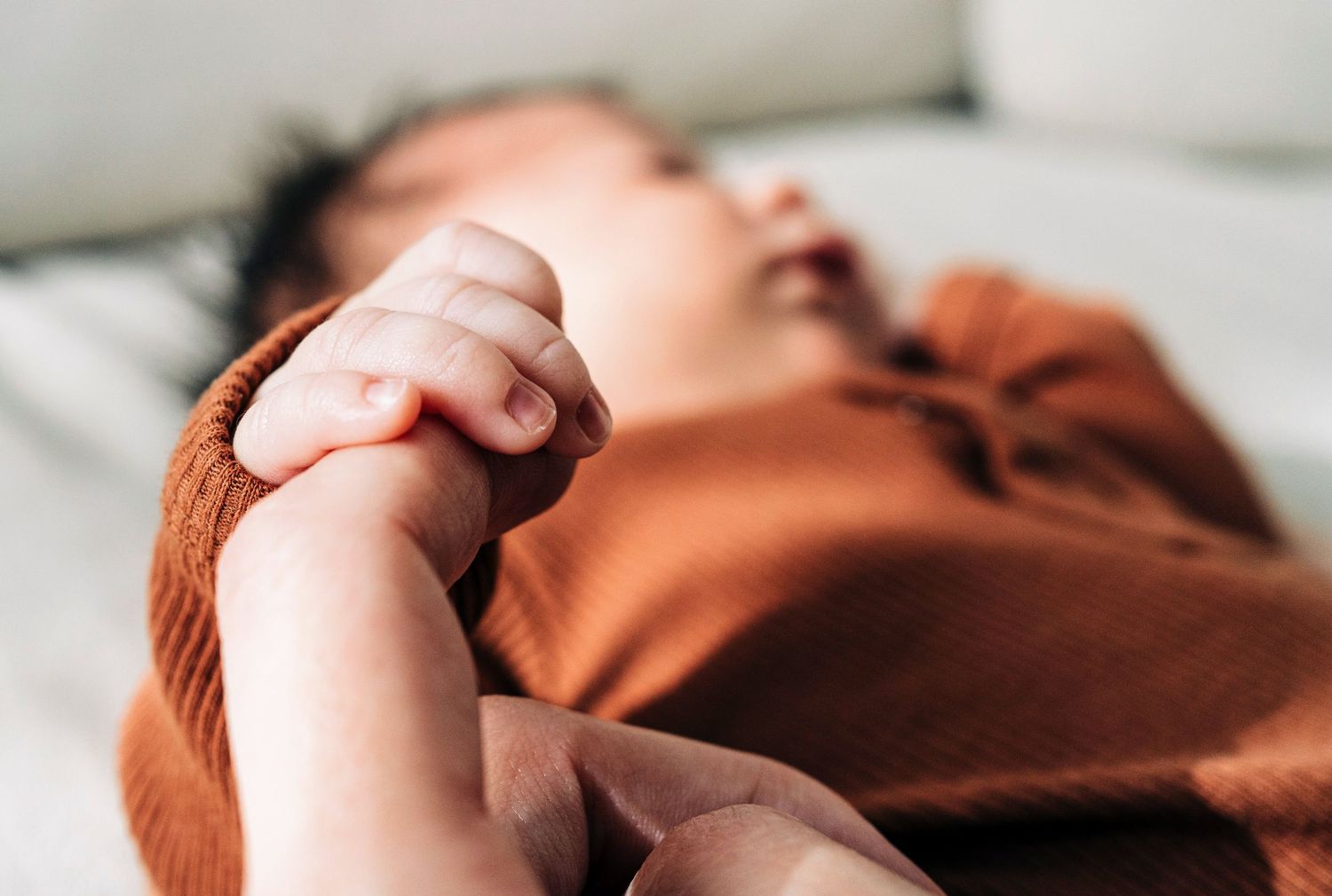 Close-up view of infant holding adult finger and warm tones in a relaxed indoor setting.
