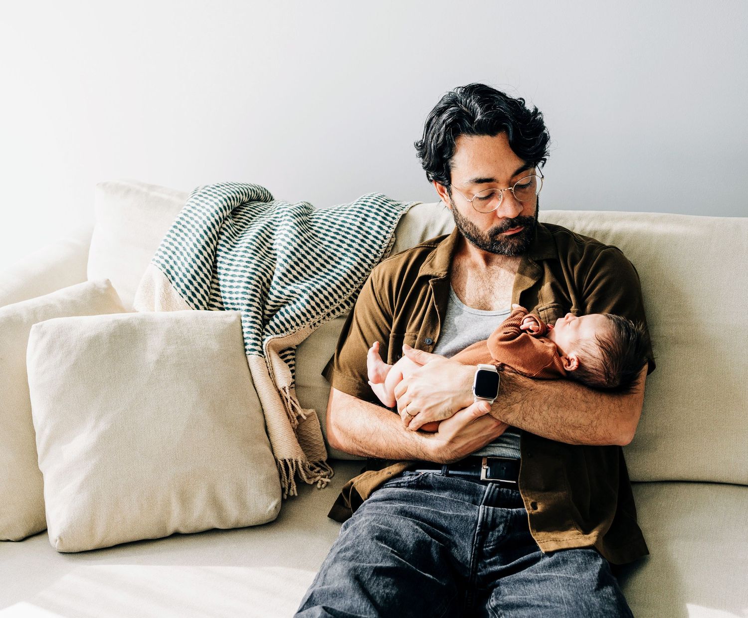 Tender moment of affection between father and newborn on a white couch in soft natural lighting.