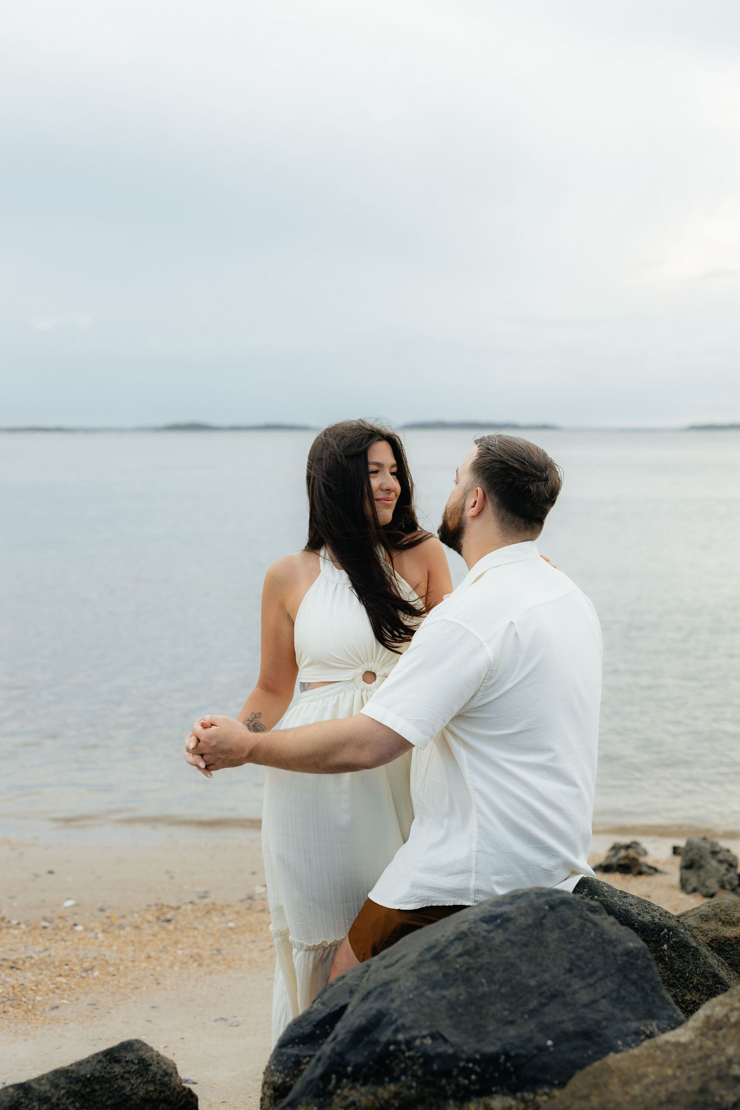 A couple sharing a tender moment on dark coastal rocks by the Fort Clinch State Park ocean.