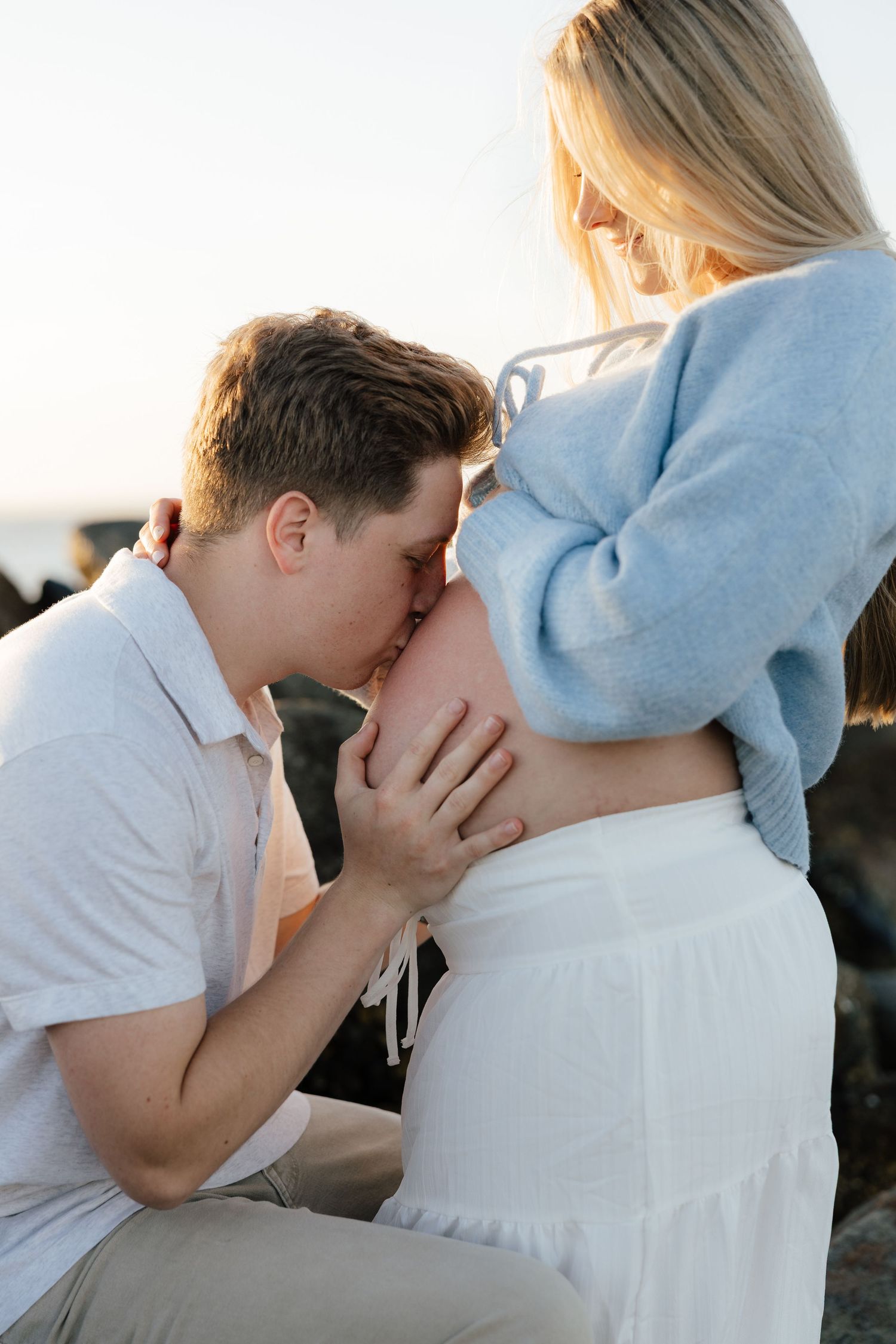 Intimate maternity photoshoot shows expectant couple sharing tender moments on the beach at sunset.