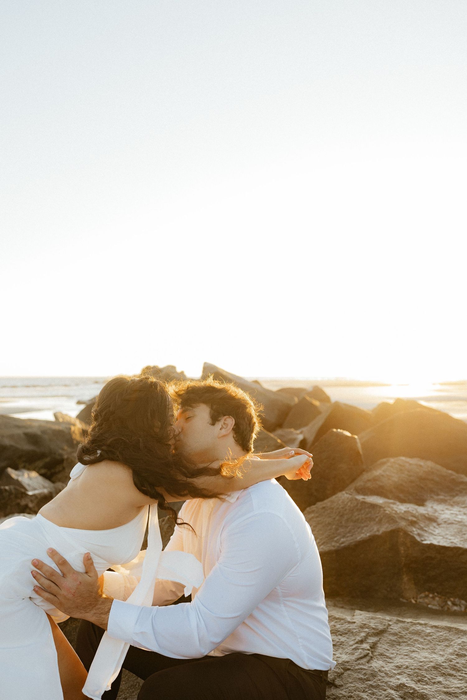 Romantic couple embracing on rocky beach at sunrise with ocean waves behind them at Fort Clinch State Park.