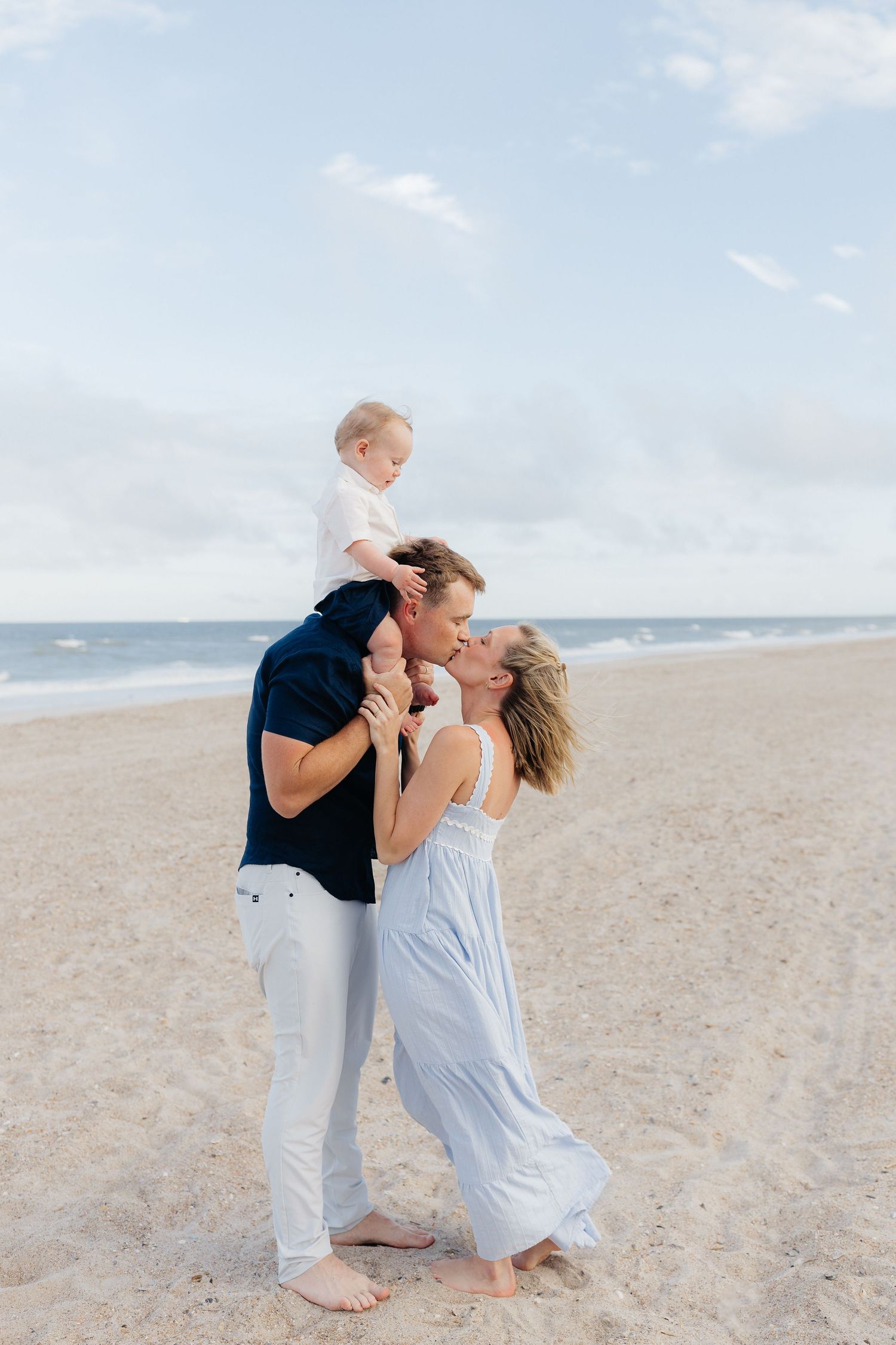 Family shares playful moment on beach with toddler riding on shoulders.