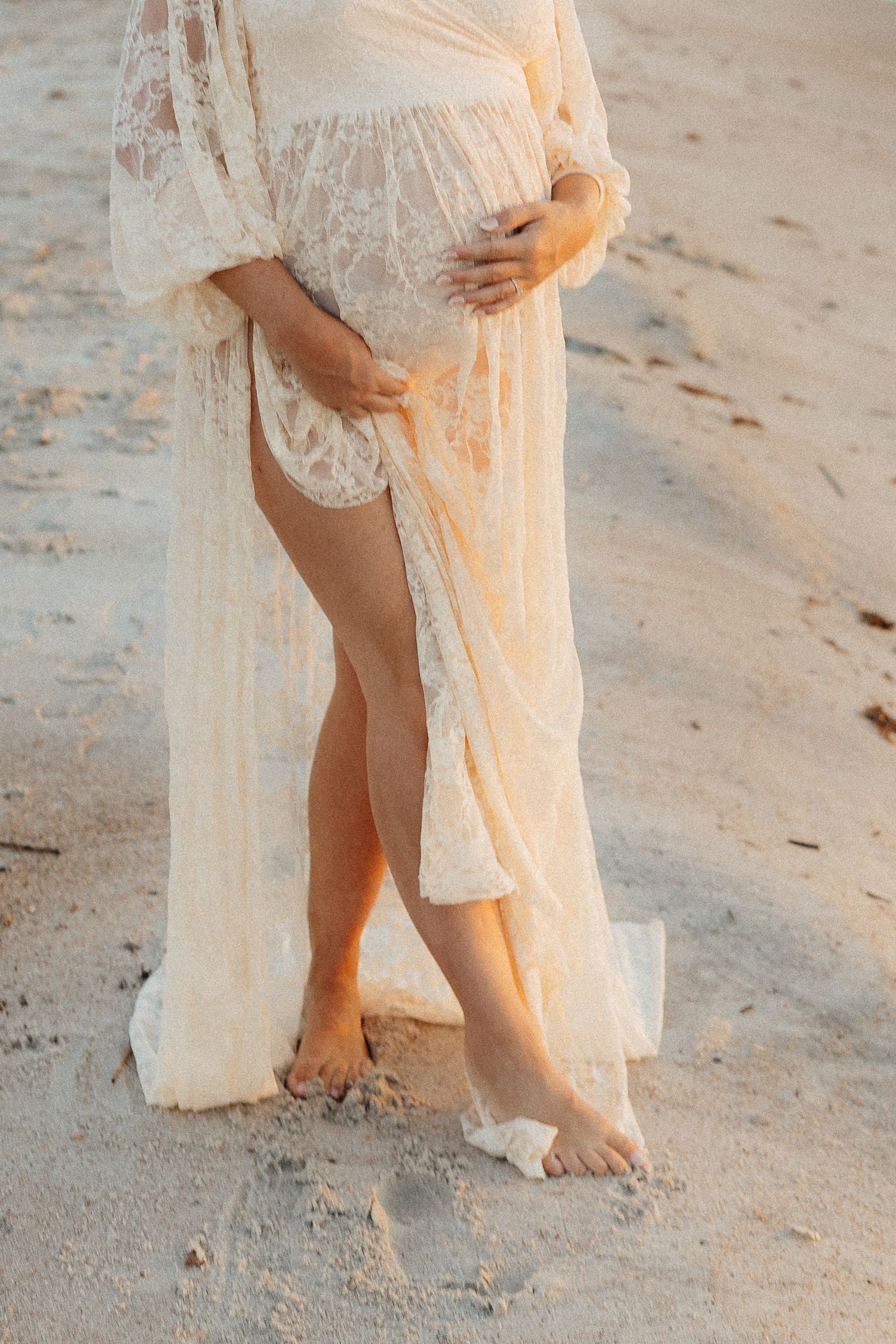 Detail shot of bare feet and lace dress hem on sandy beach.