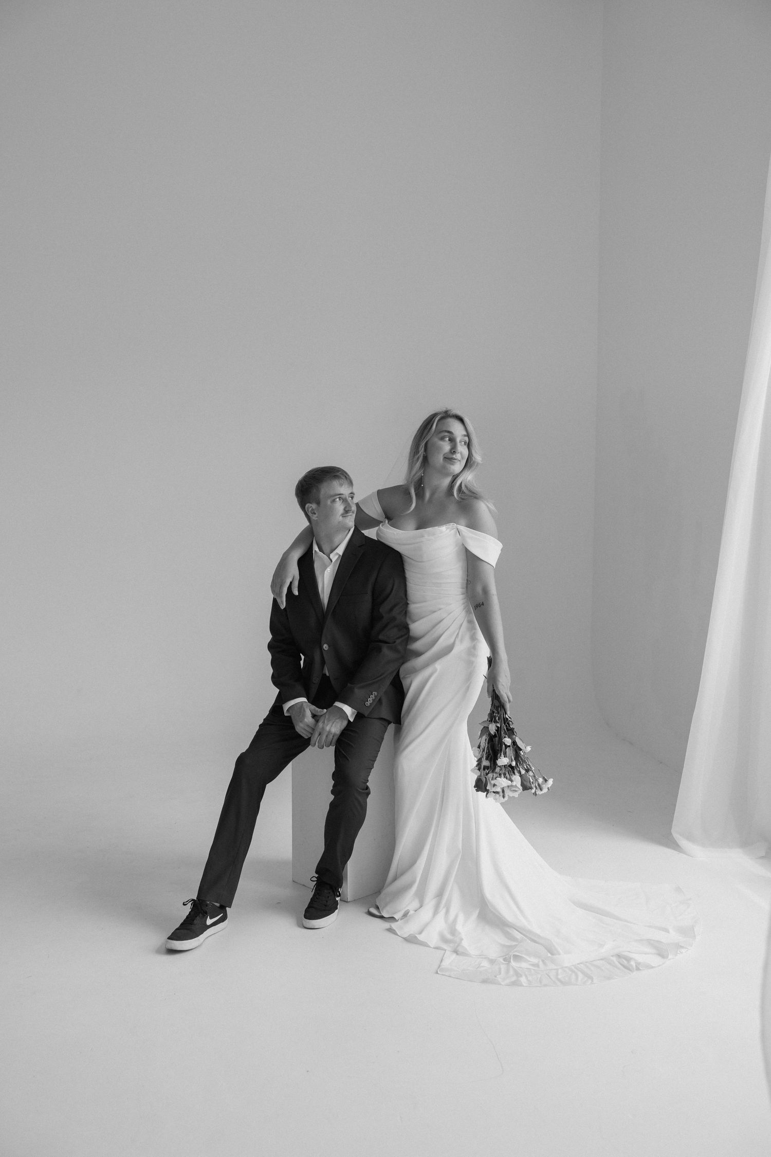 A studio portrait of a couple in wedding attire posing against a white background.