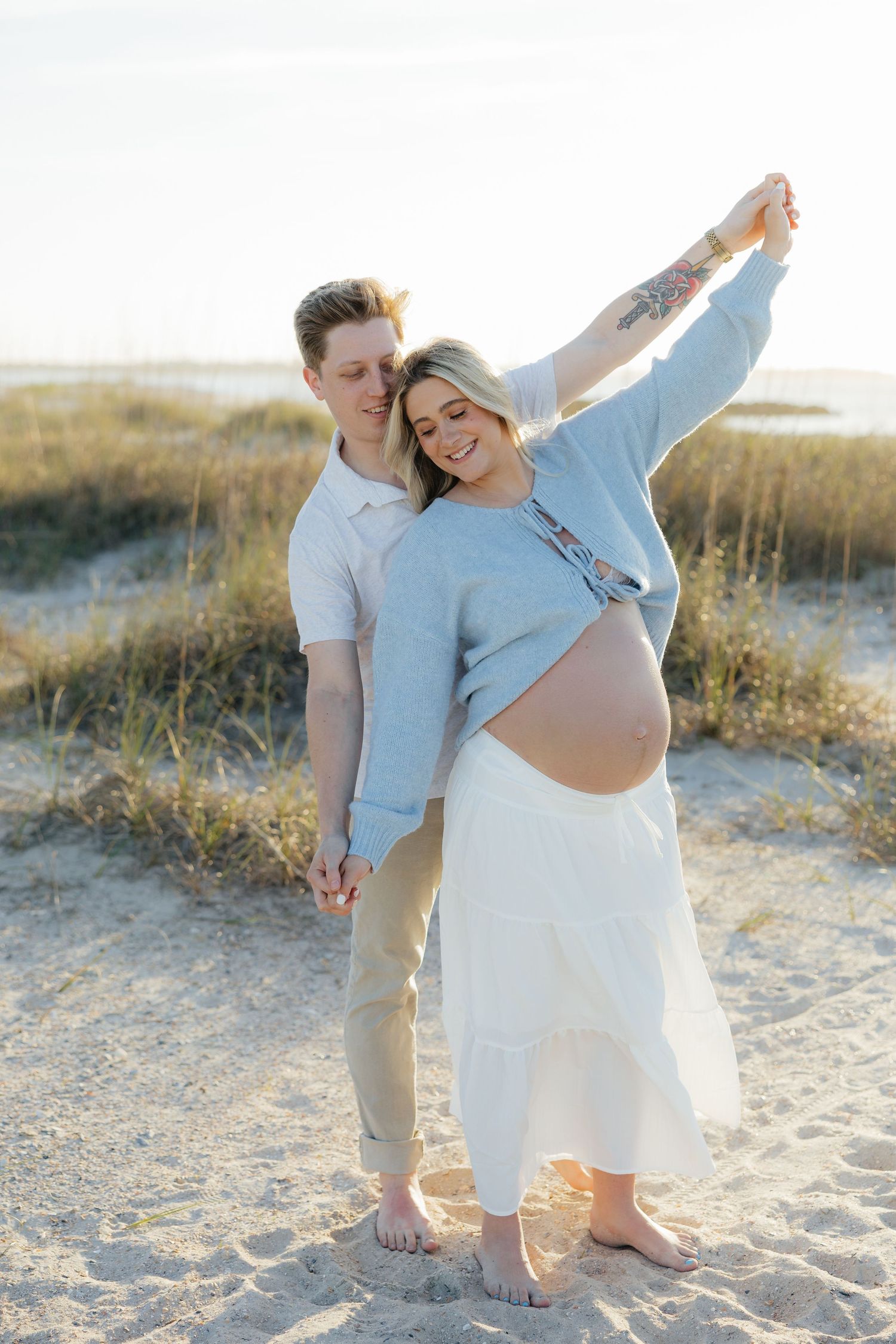 A couple shares a tender moment together on a sandy beach during sunset, creating a romantic coastal atmosphere.