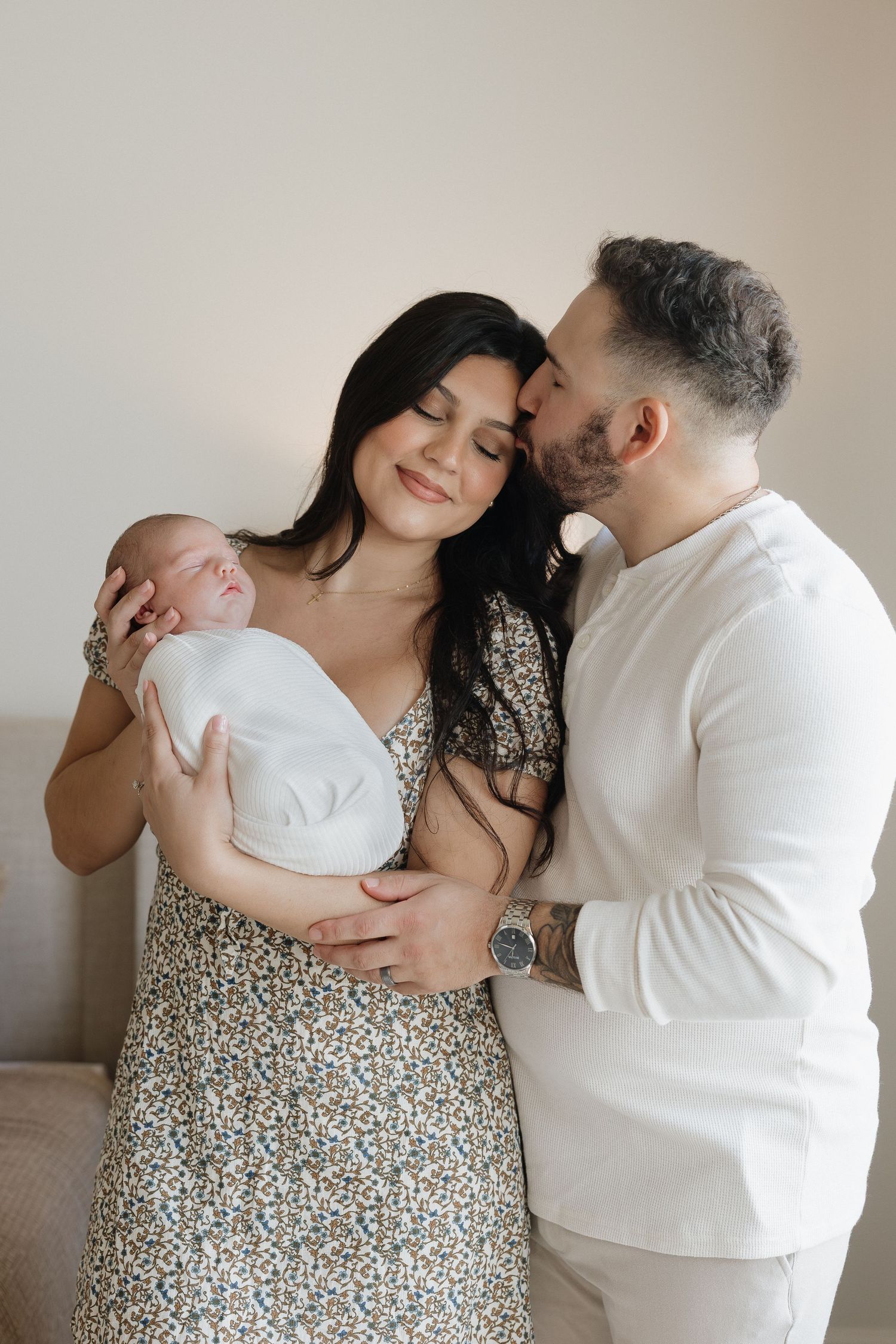 A couple in white and floral dress share tender moments with their newborn baby in a series of intimate photos.