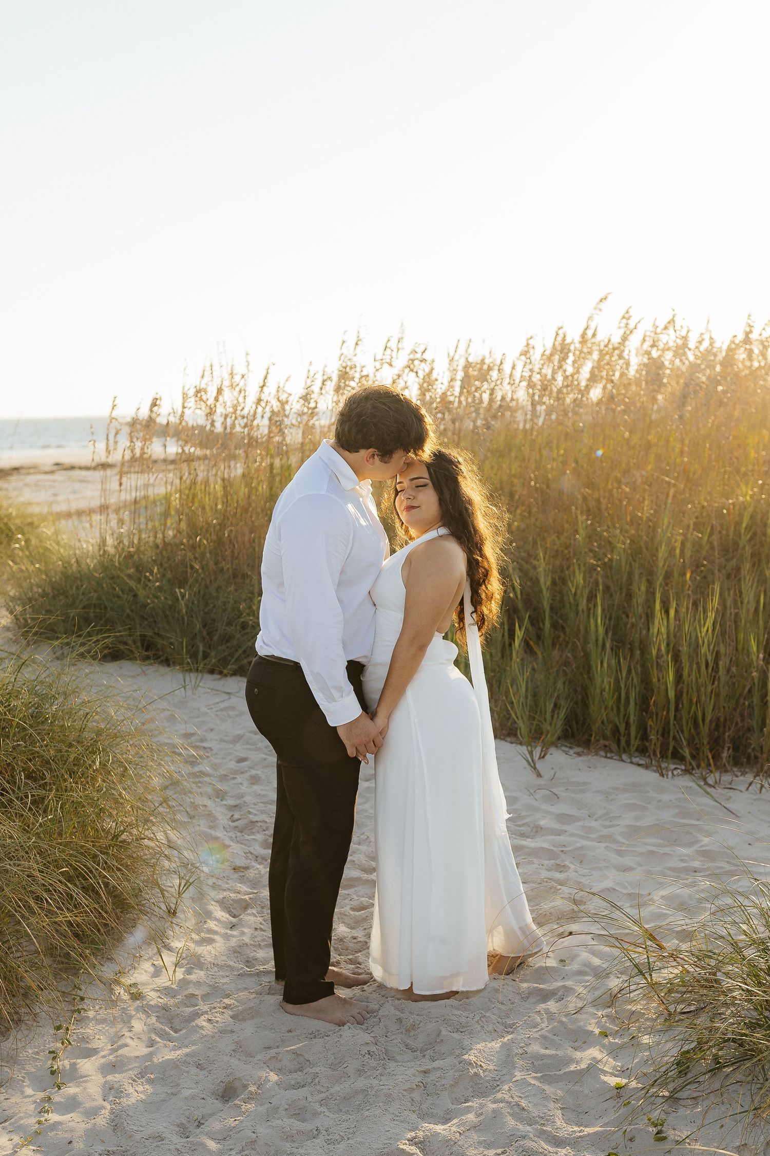 Romantic beach photoshoot among sea grass during golden sunset.