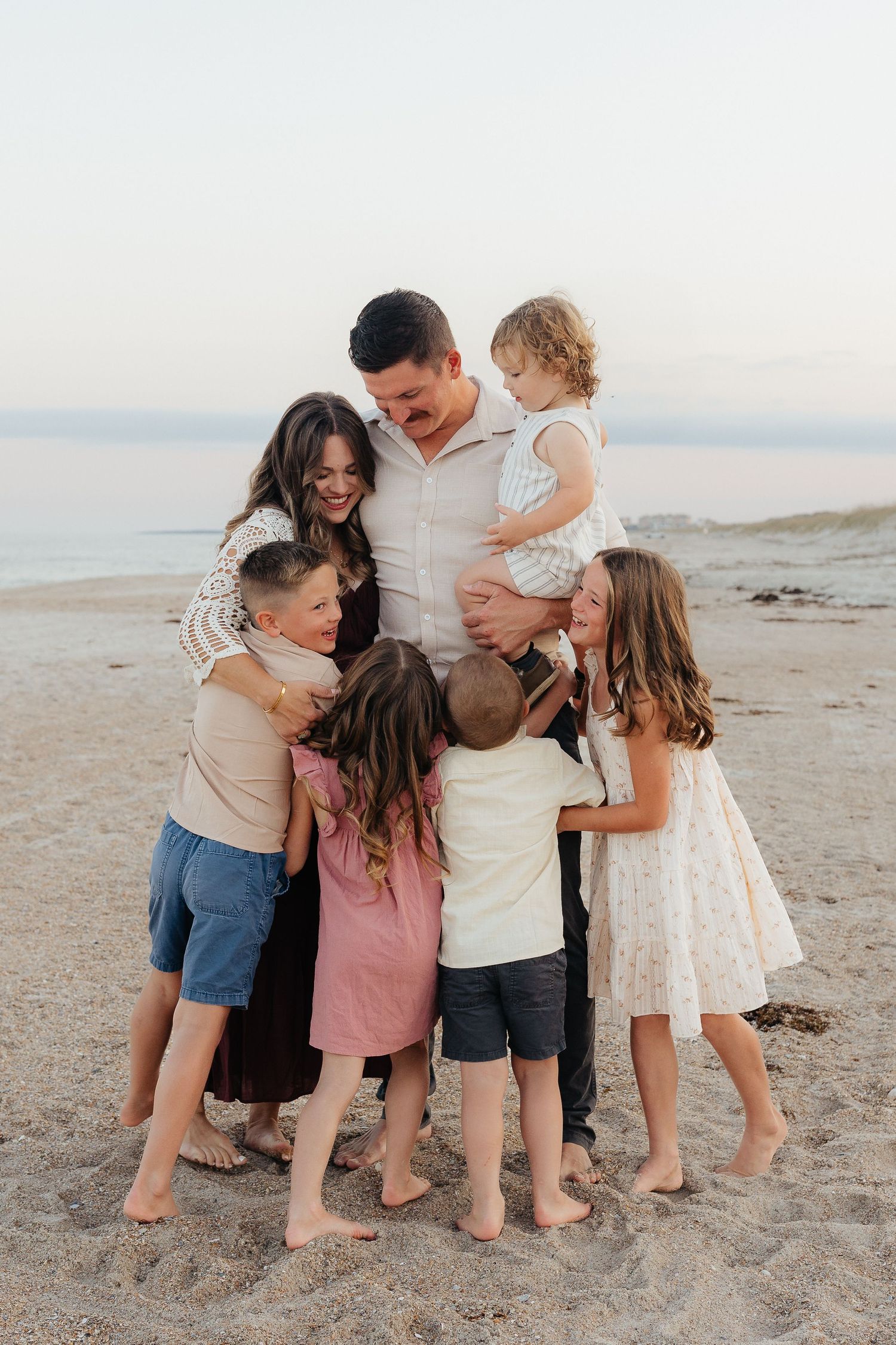 Happy family shares group hug on beach at sunset creating heartwarming moment.