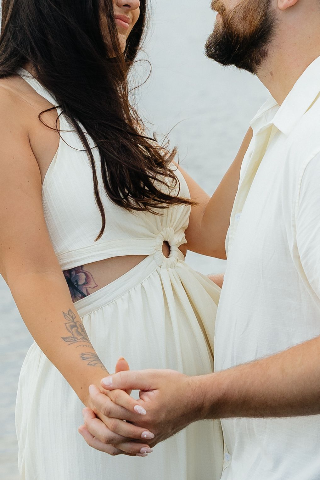 An intimate close-up of a couple in white clothing holding hands with visible tattoos.