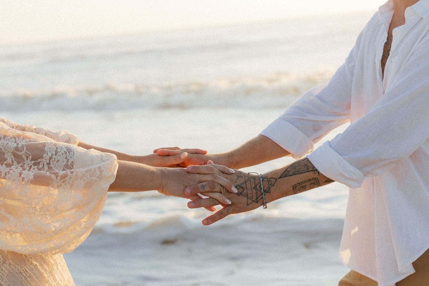 Close-up of hands with henna design holding each other against Amelia Island, Florida ocean backdrop.