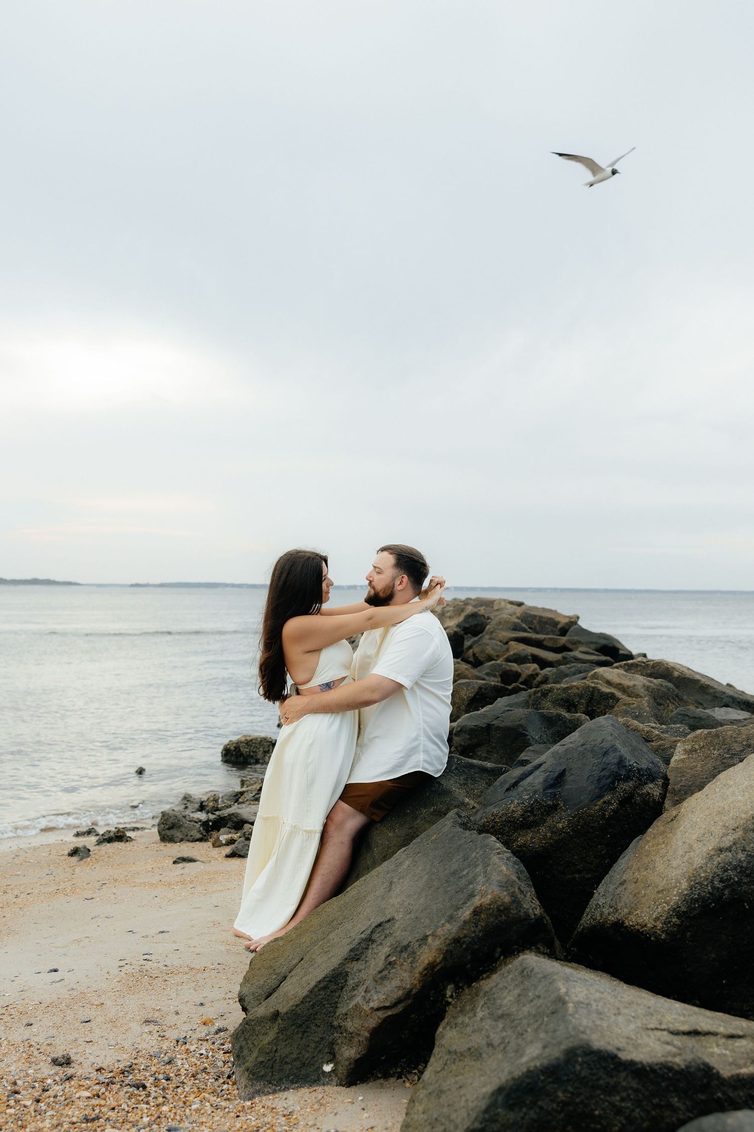 A couple embracing on coastal rocks as a seagull flies overhead in Fort Clinch State Park.