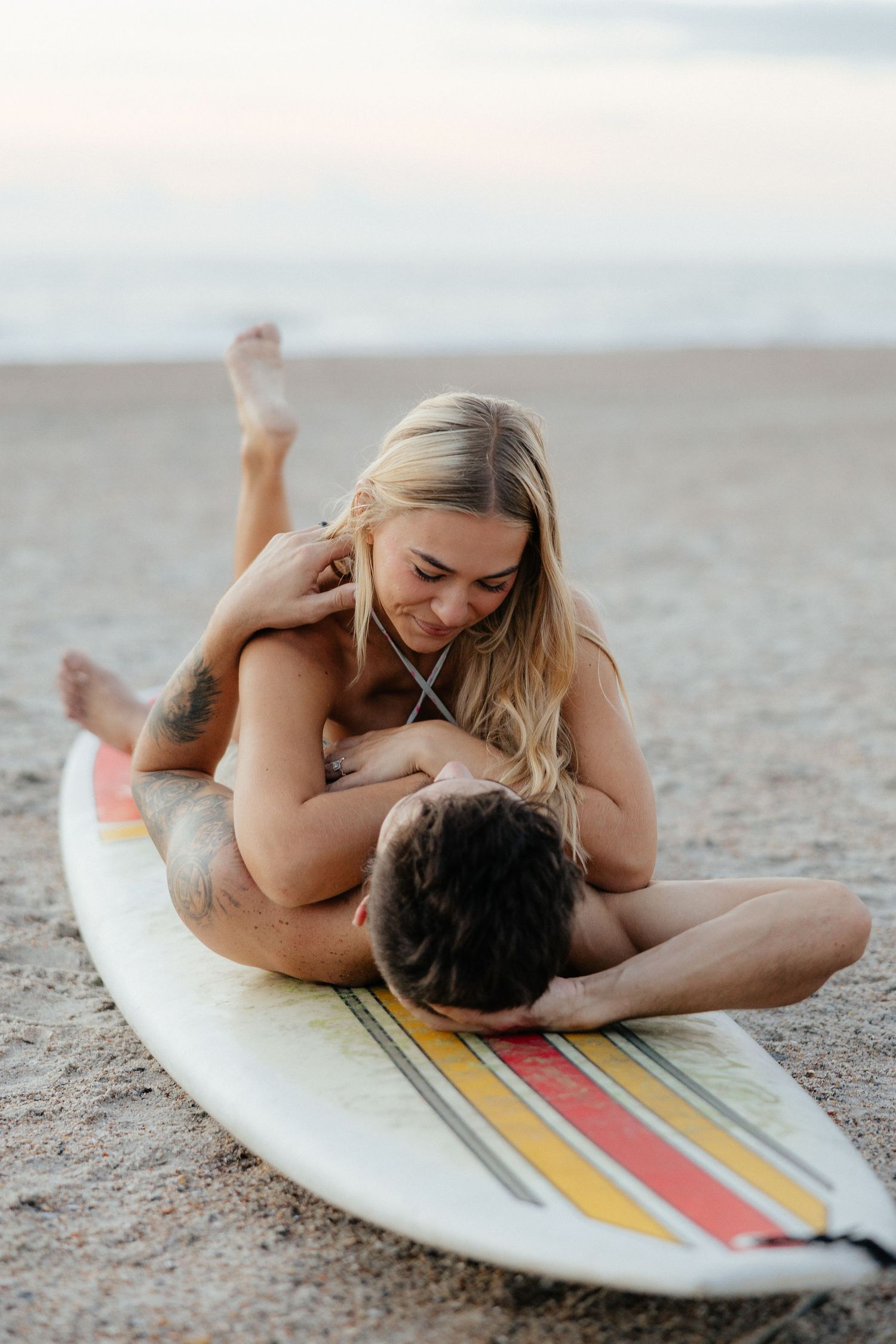 A couple sharing an intimate moment on a surfboard on the beach.