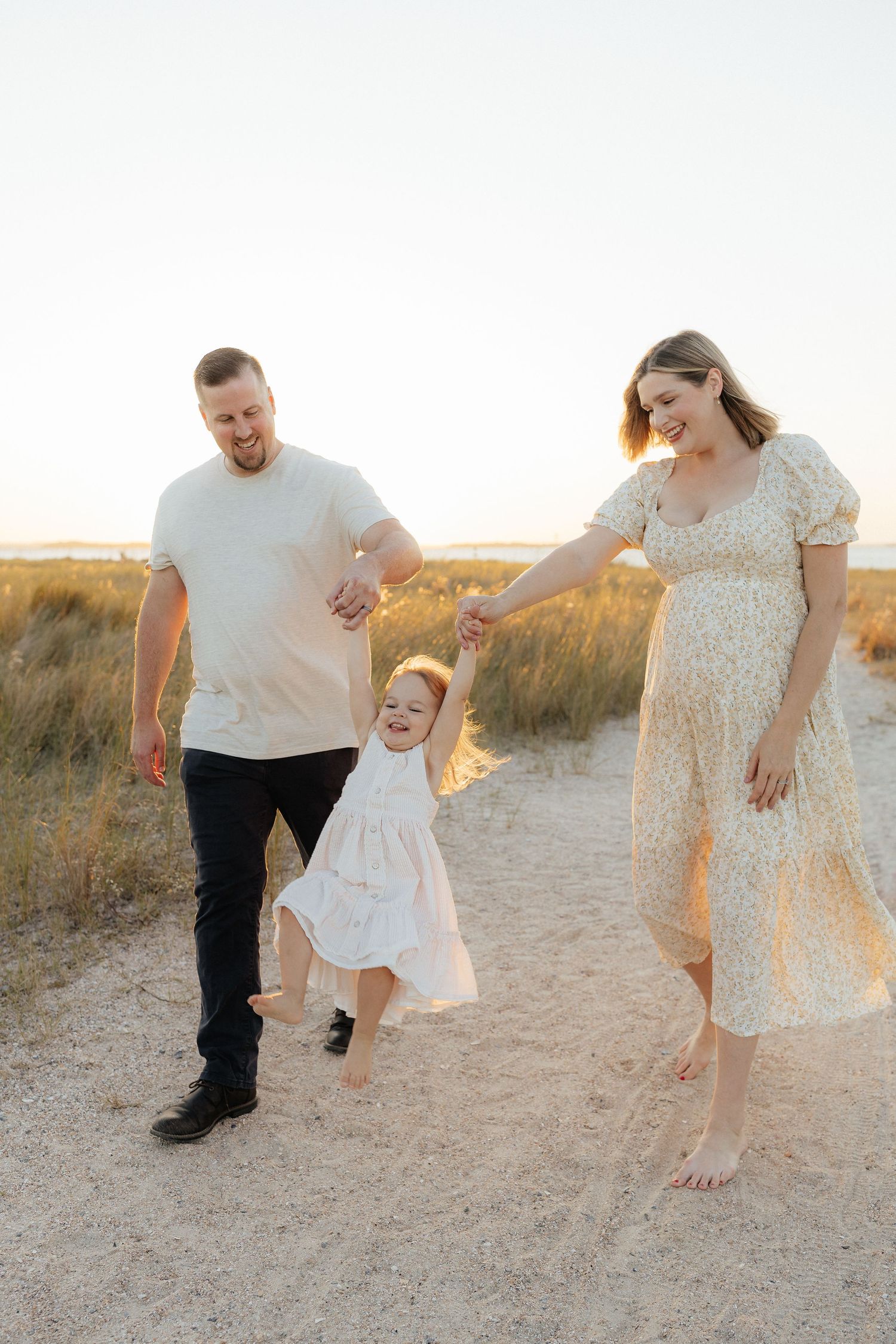 Family plays and dances together on sandy Fort Clinch State Park beach path during golden hour photoshoot.