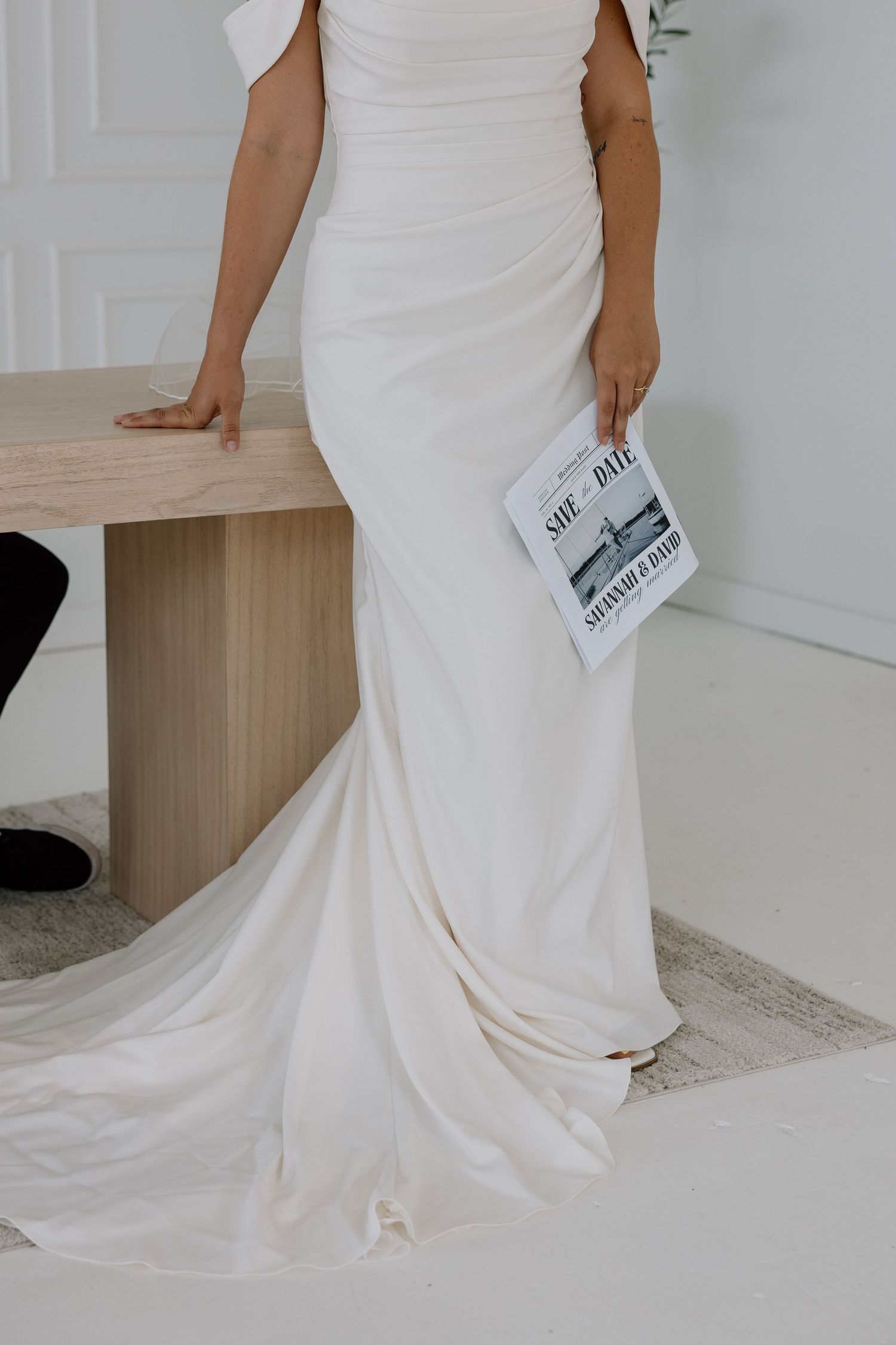 Detail shot of a flowing white wedding dress train with a save-the-date card.