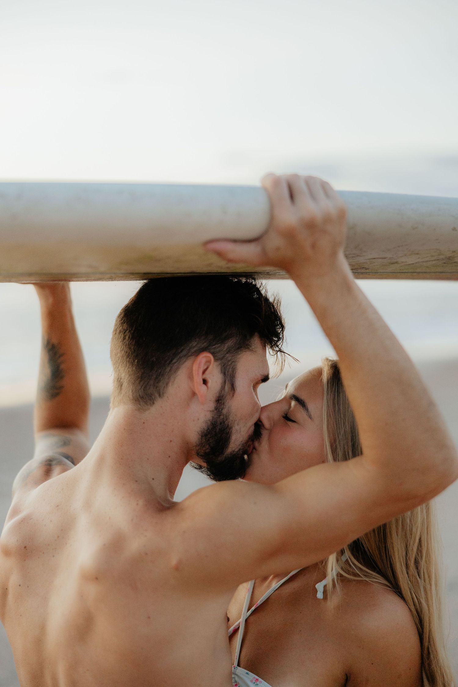 Couple sharing passionate moment beneath wooden beach structure.