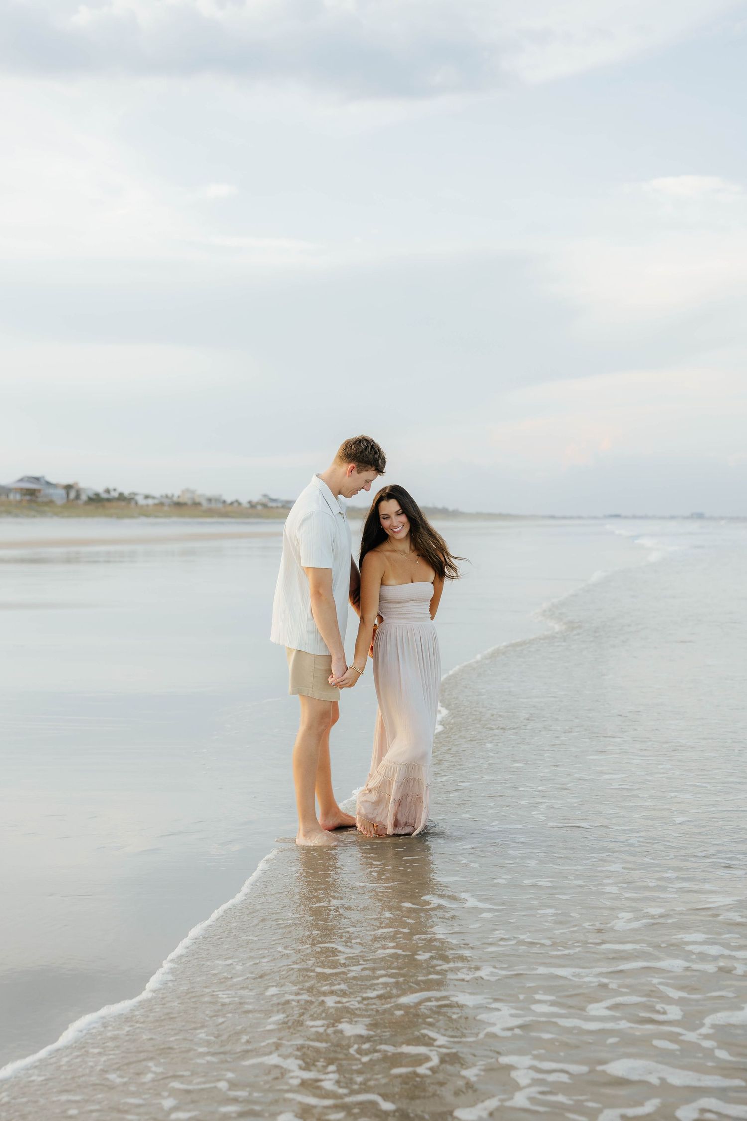 A couple wades together in shallow ocean waters during a dreamy beach photoshoot.