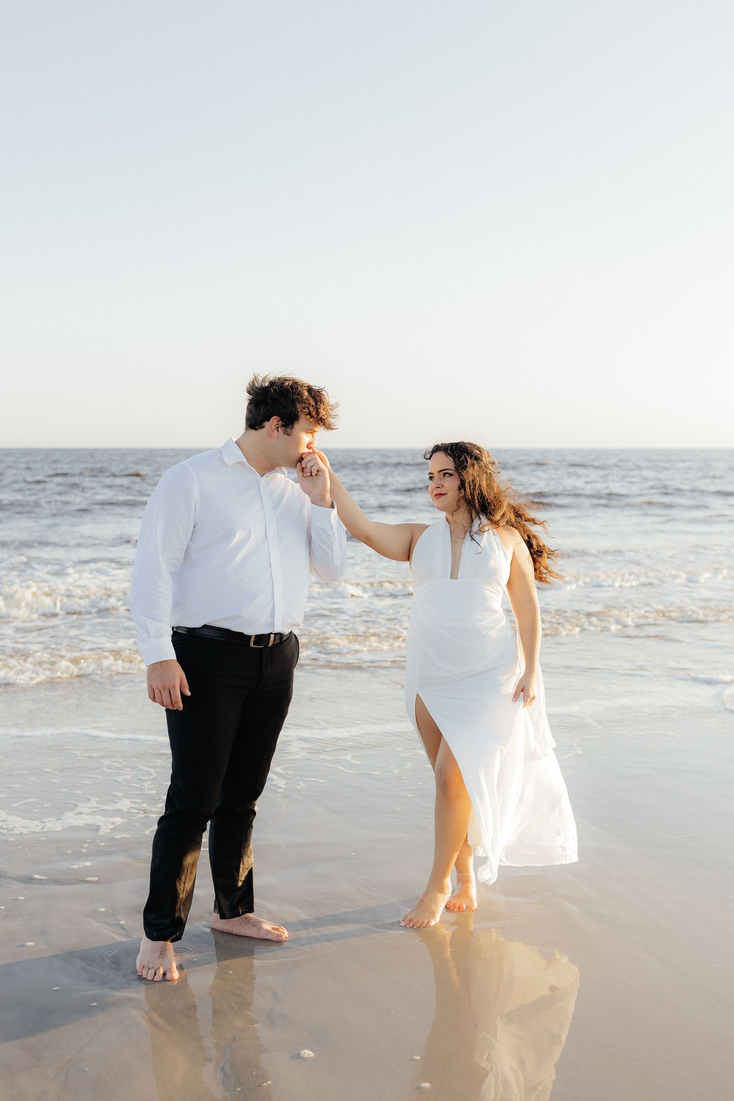 Couple in white and black attire playfully dancing in the ocean waves at Fort Clinch State Park.