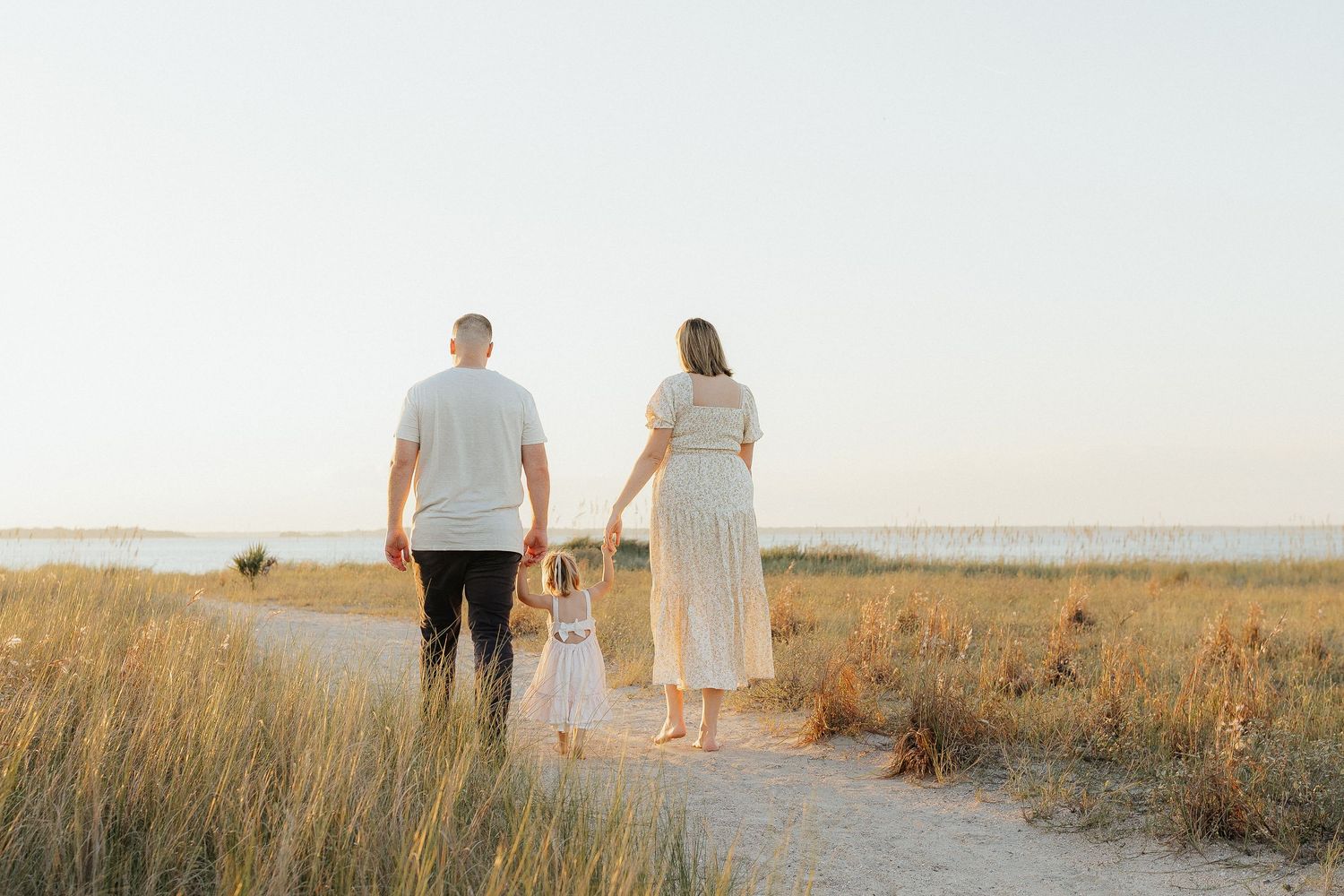Couple walking together through a golden field at sunset with mountains in the background in Fort Clinch State Park.