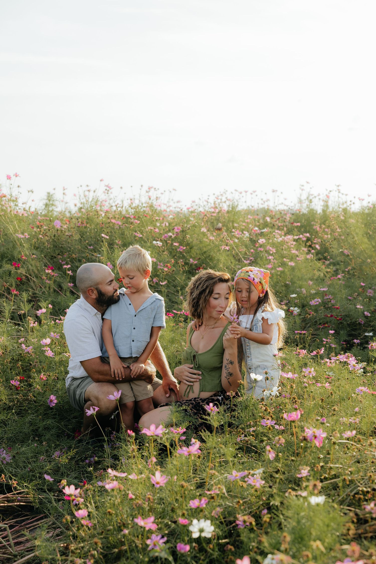 Family sits together among blooming pink wildflowers in a summer meadow.