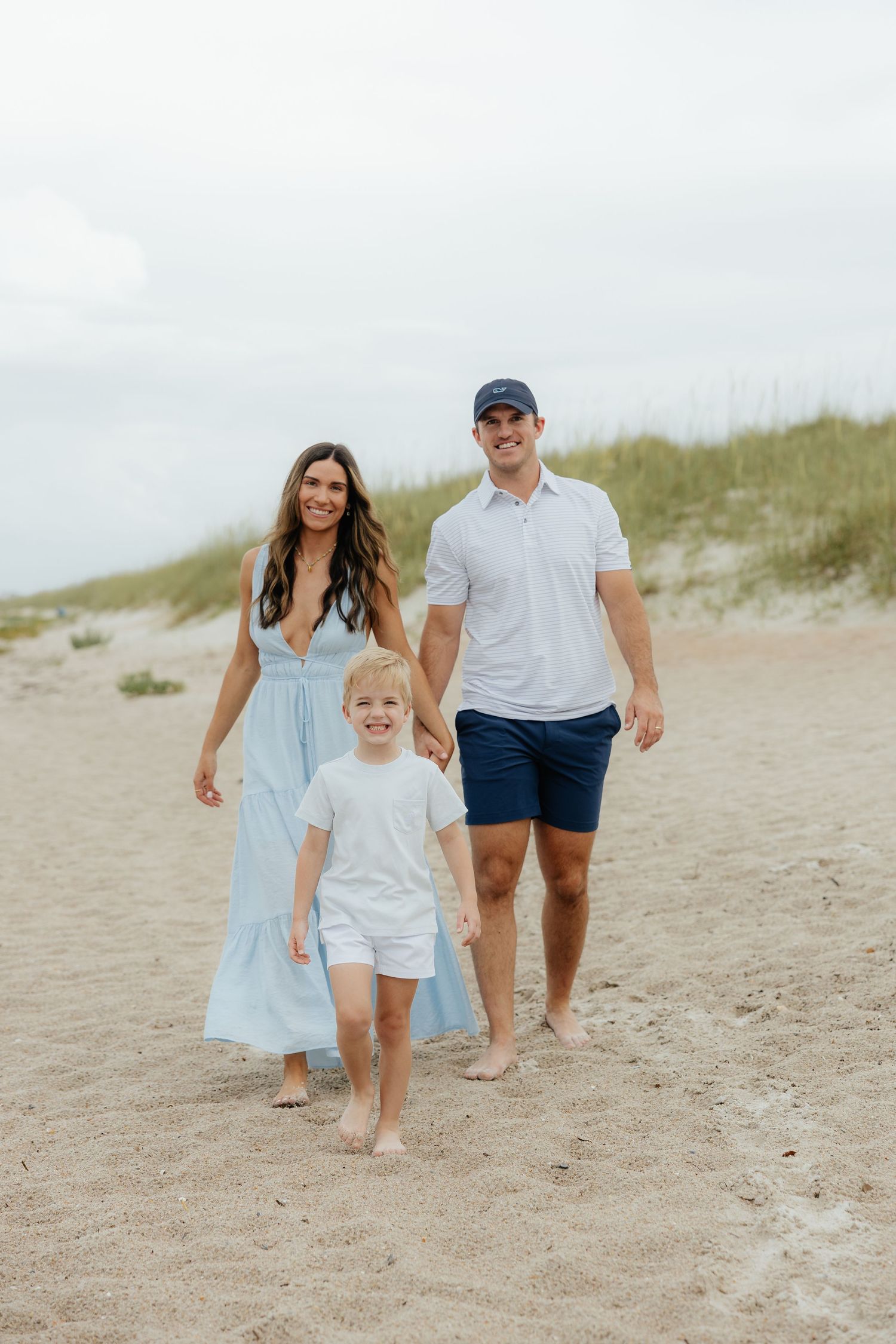 A family walks barefoot together on the Ritz-Carlton, Amelia Island beach with sand dunes in the background.