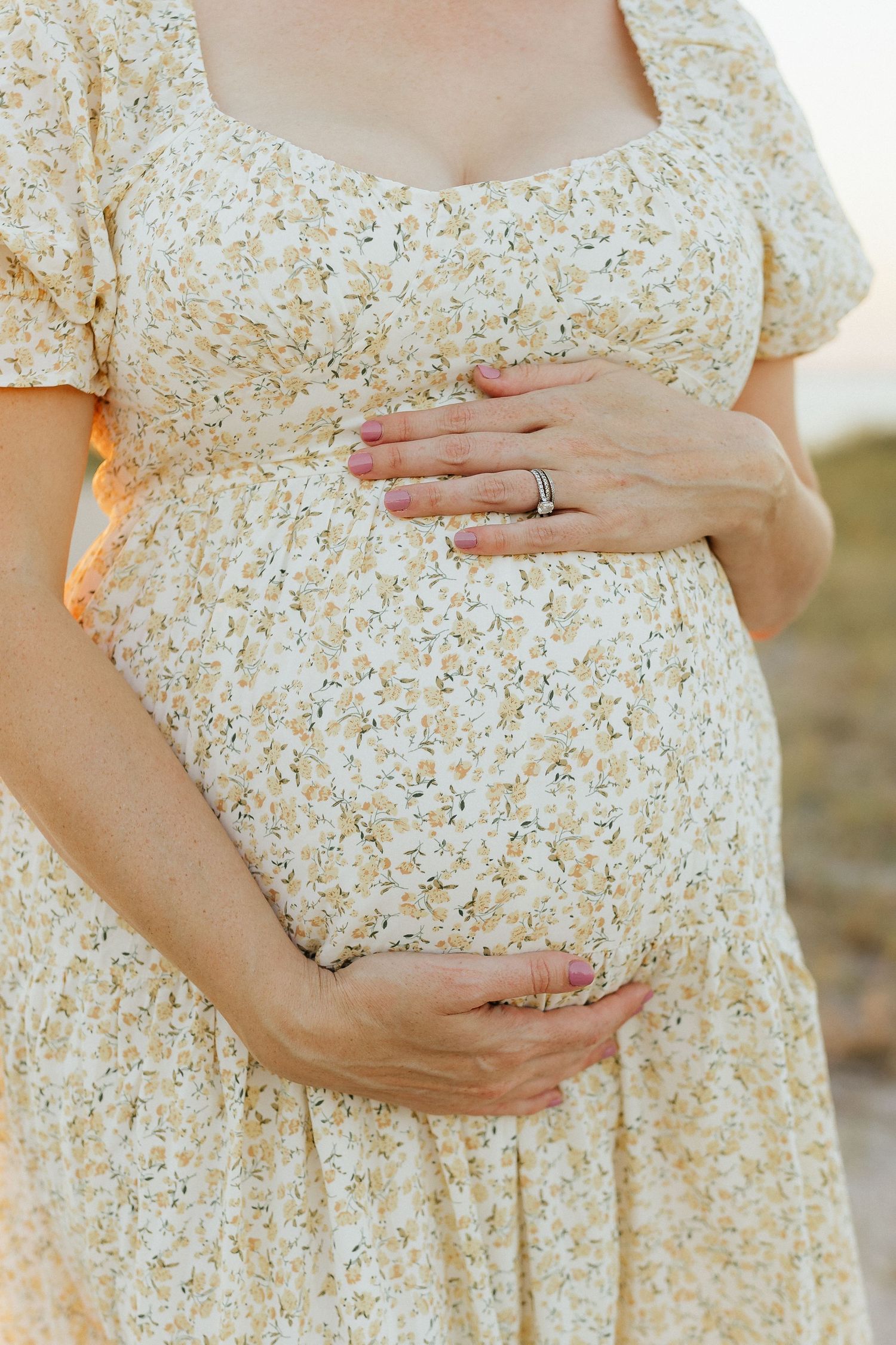 Close-up shots of hands tenderly cradling a pregnant belly in a floral dress in Fort Clinch State Park.