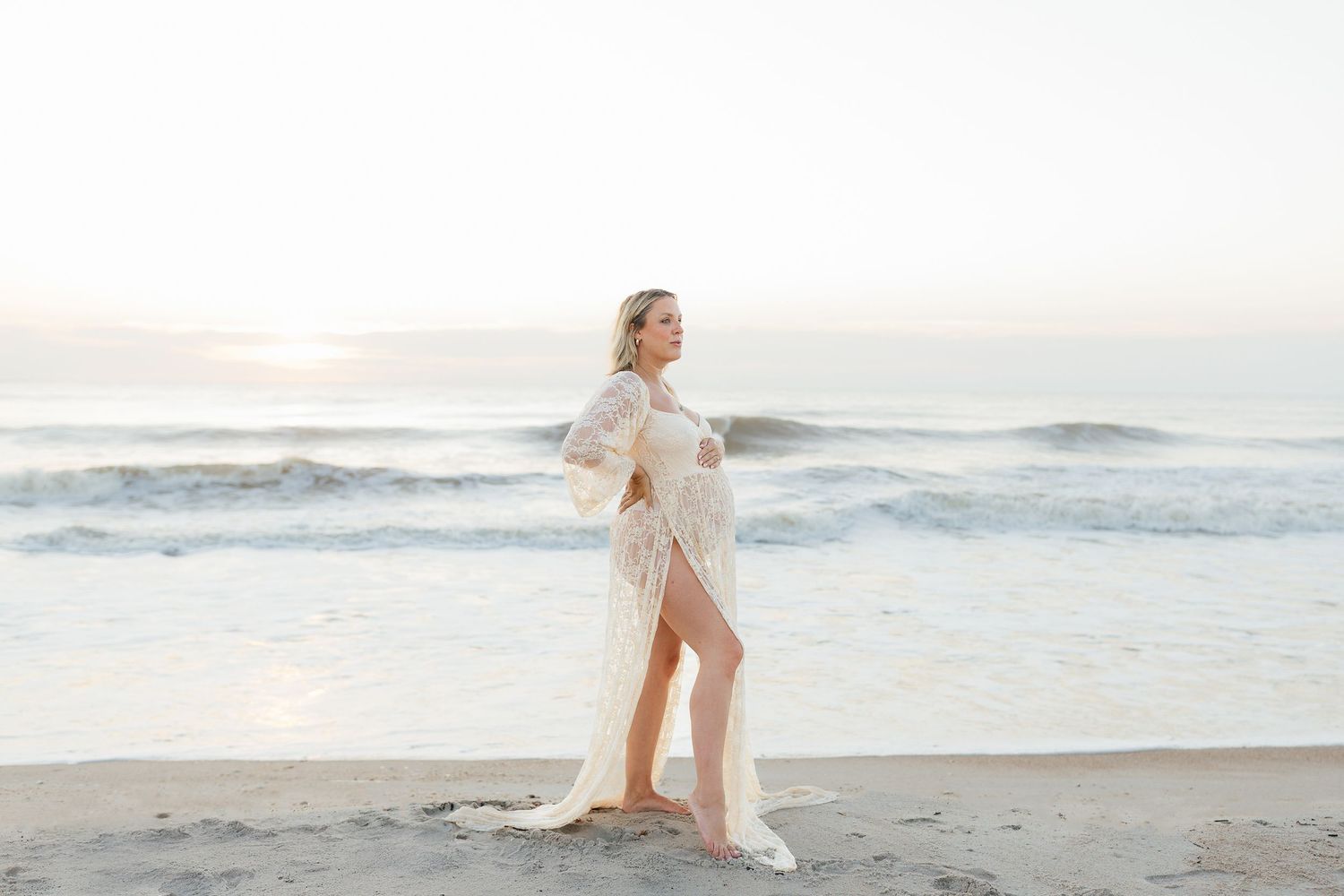 Couple in elegant attire embracing on a serene beach at sunset with waves crashing in the background.