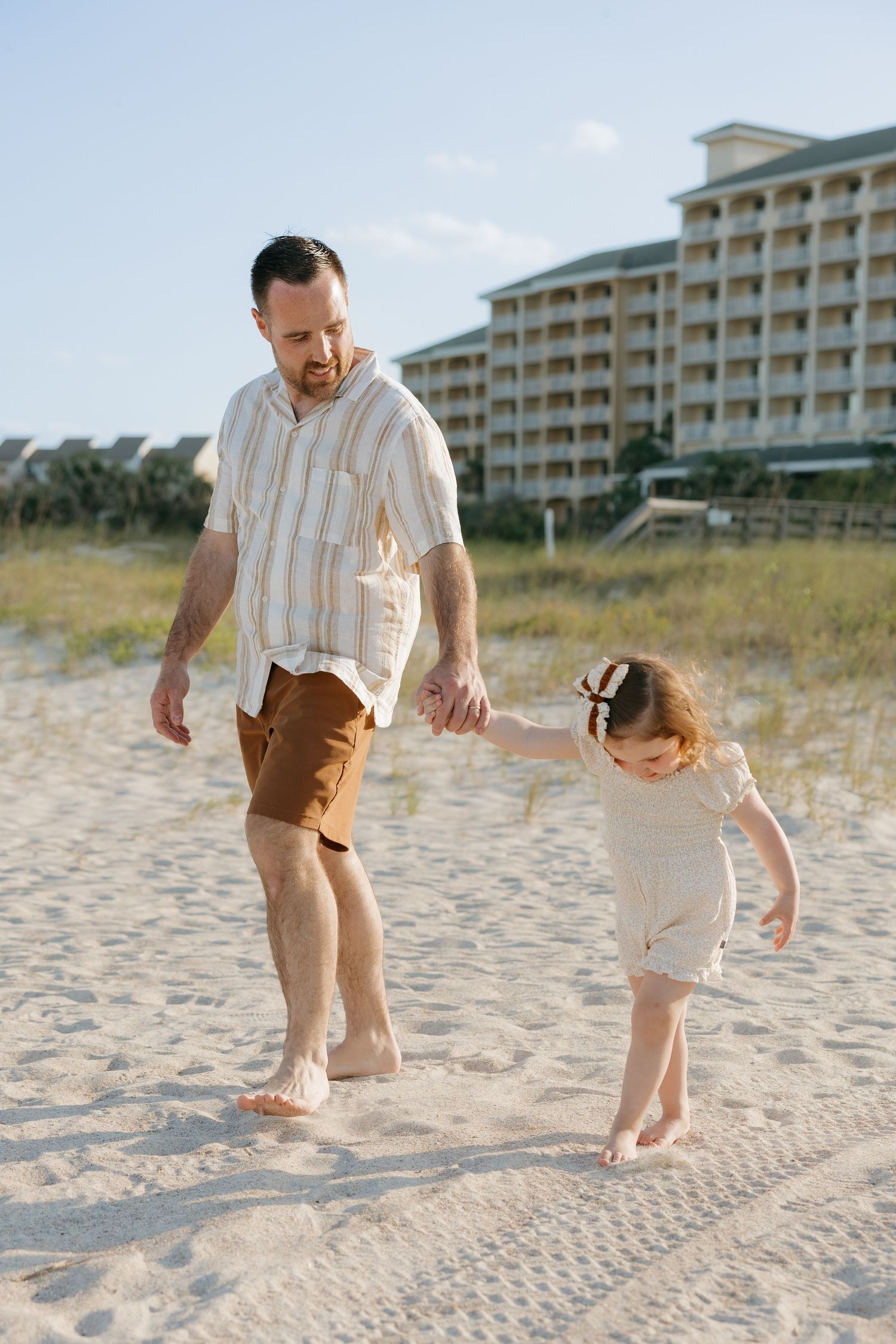 A parent and child walk together on sandy beach with resort building in background at Omni Amelia Island Resort & Spa.