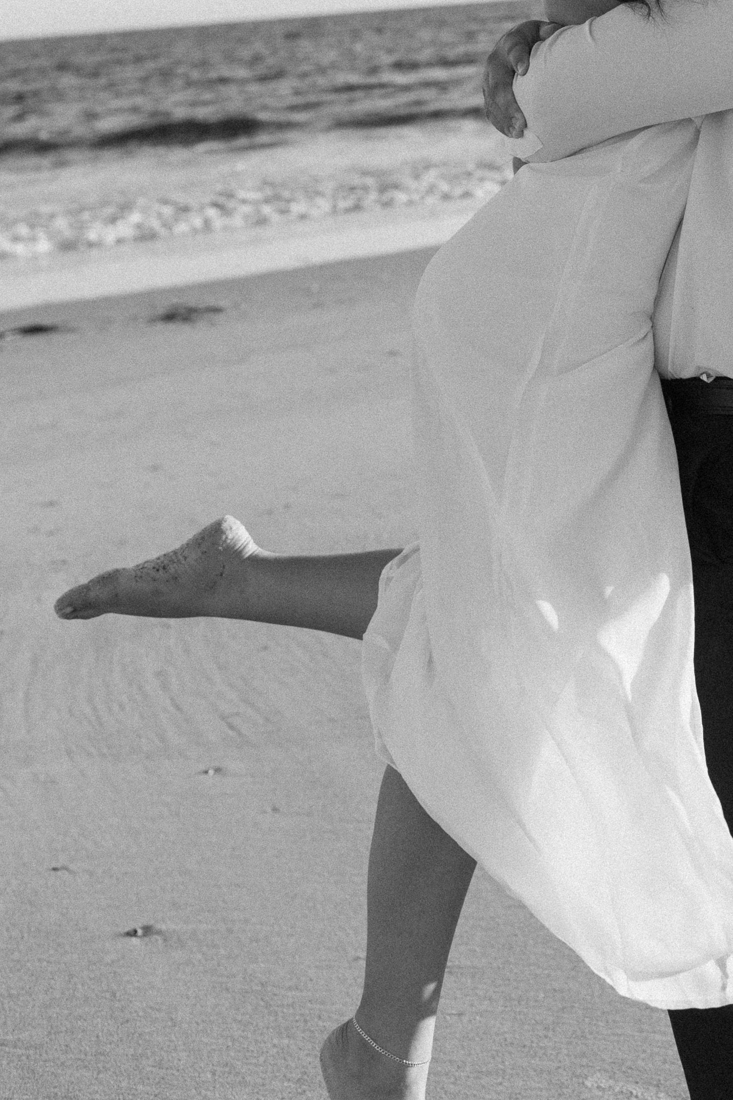 Flowing white dress catches the ocean breeze during beach photoshoot.