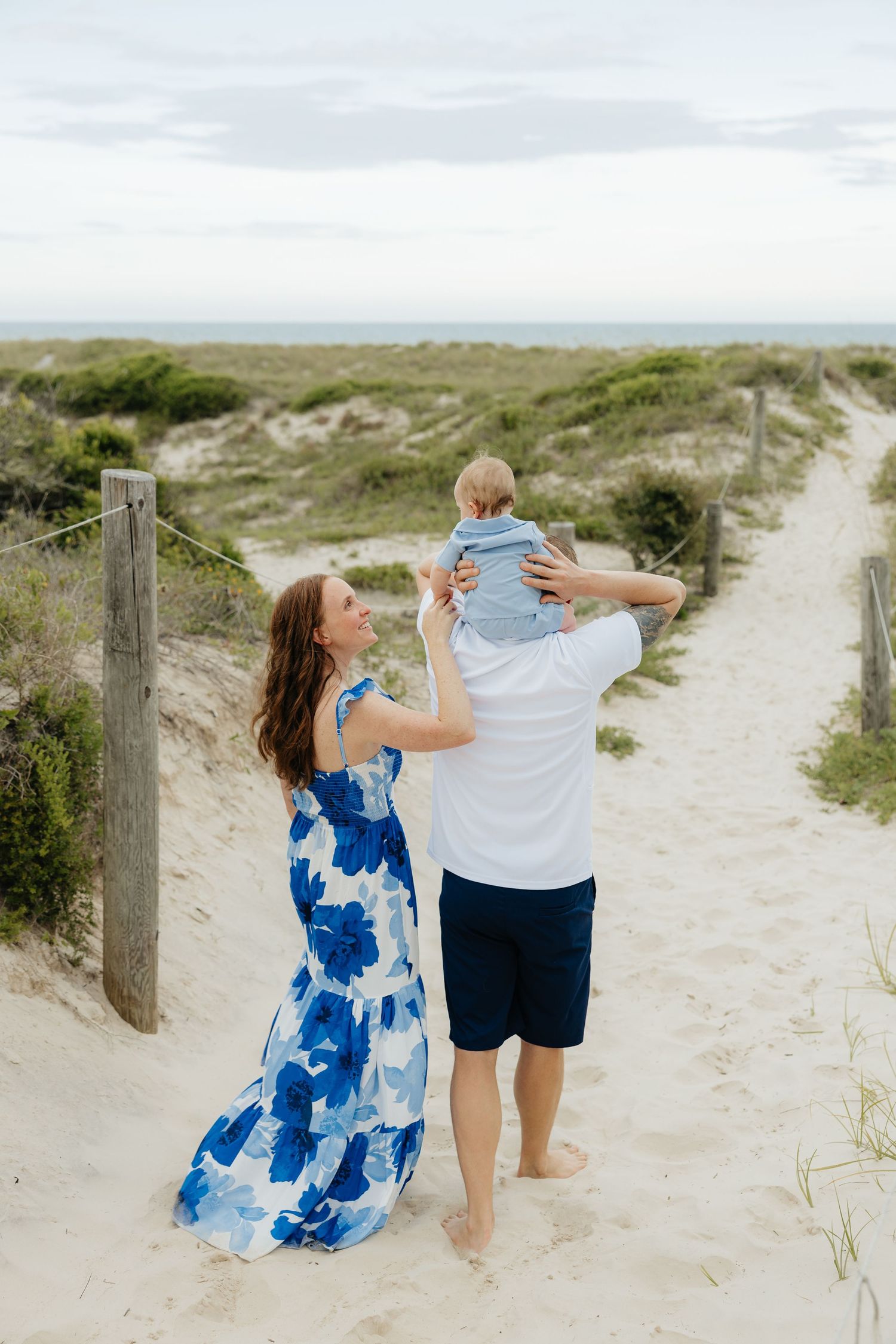 Family enjoying a moment together on sandy beach path through coastal dunes.