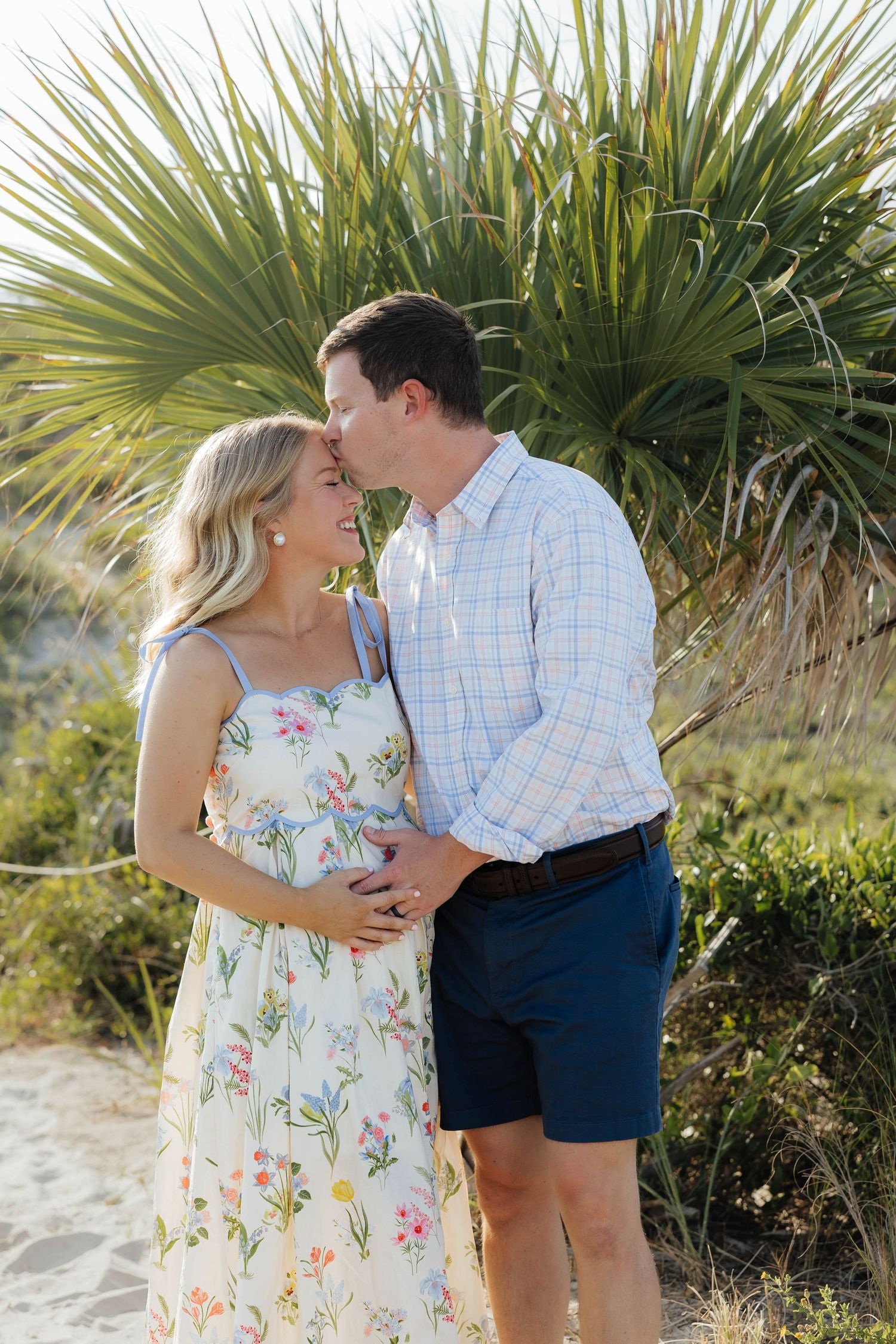 A romantic couple embraces near palm trees on a sunny beach path in summer.