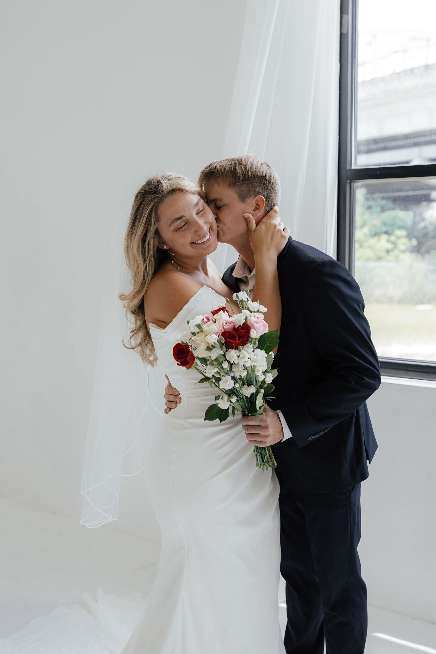 A romantic wedding photoshoot featuring a bride and groom near a window.
