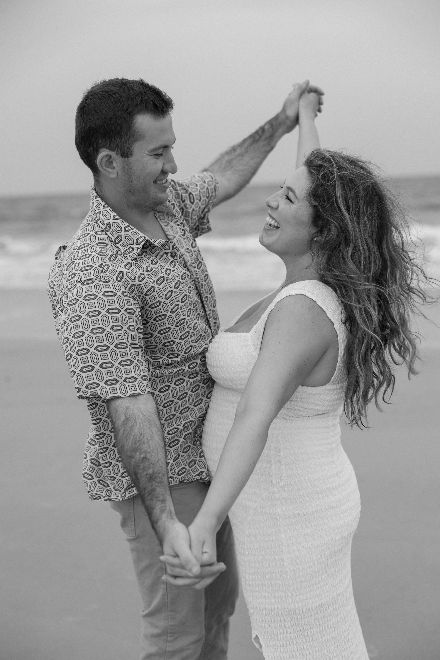 Couple sharing joyful dance moves on beach with waves in background.
