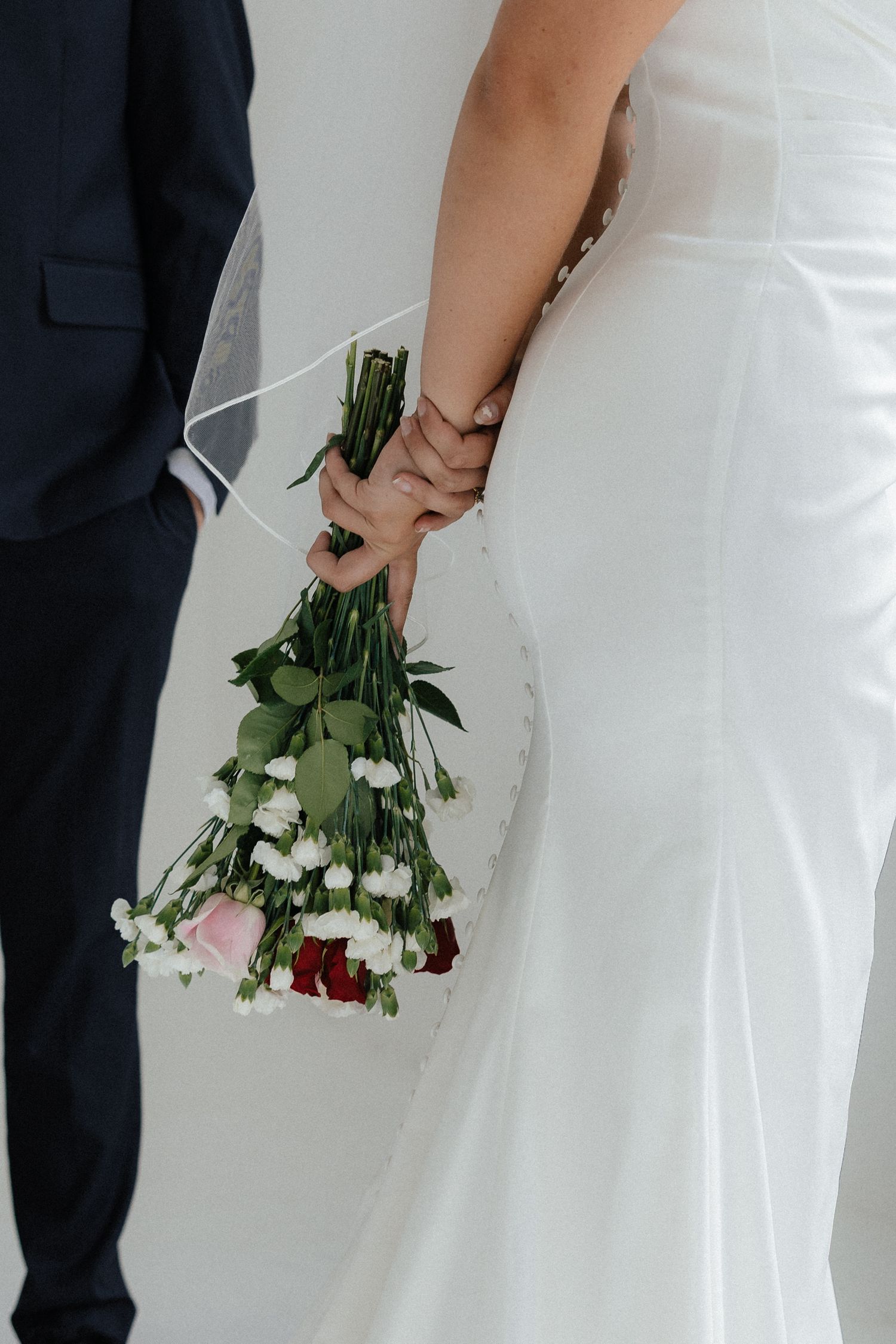 A cropped view of a bride holding a delicate bouquet of pink and white flowers.