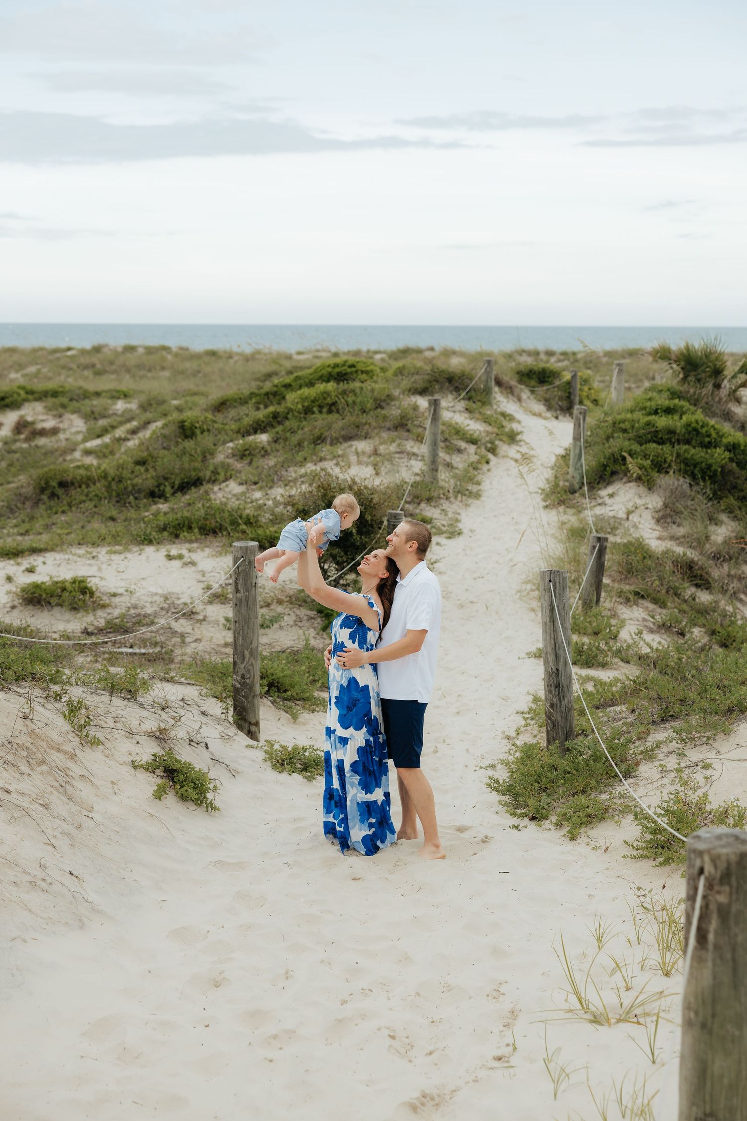 A family shares a joyful moment on a coastal boardwalk surrounded by sand dunes and ocean views.