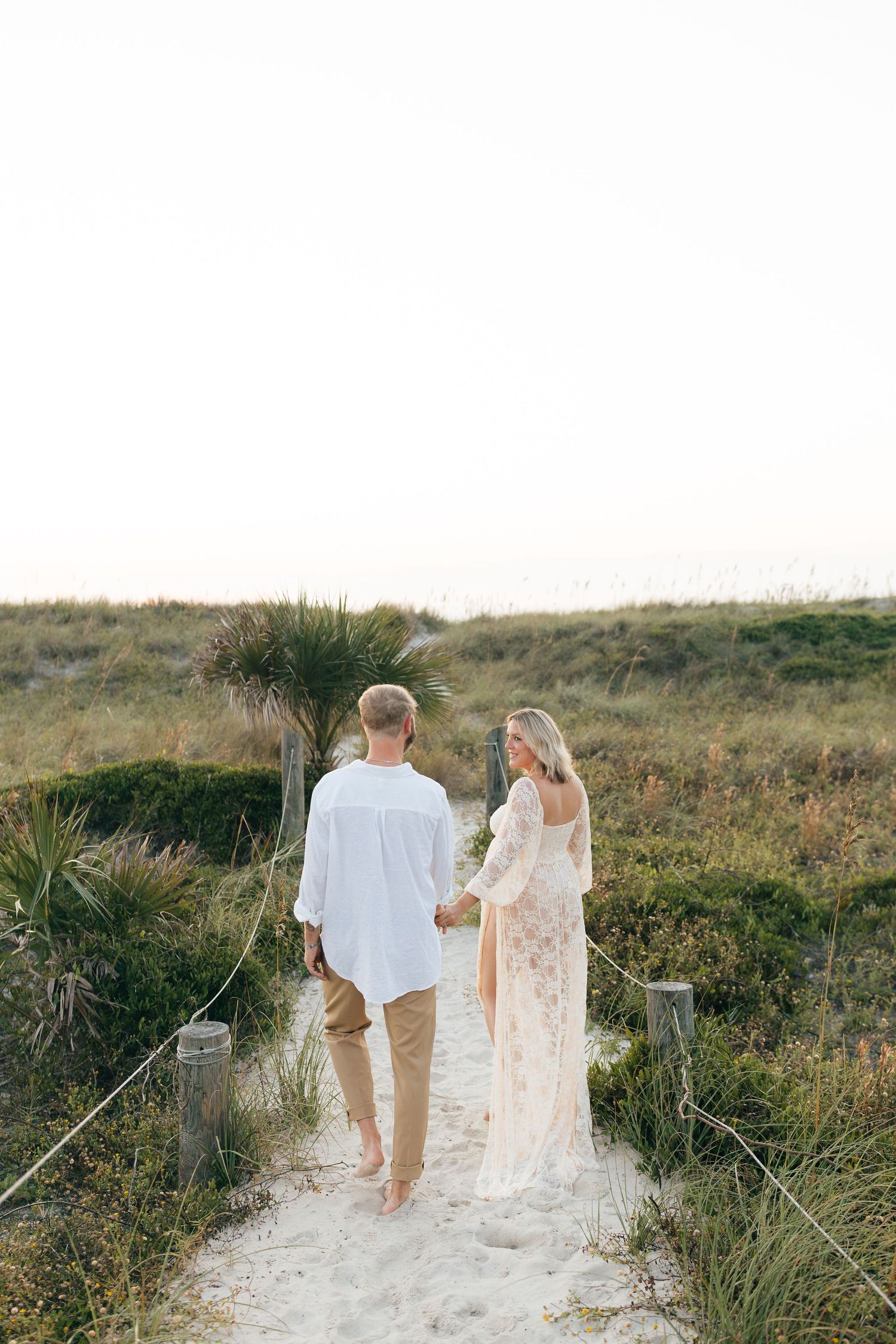 Couple walking hand in hand along sandy beach path at sunset.