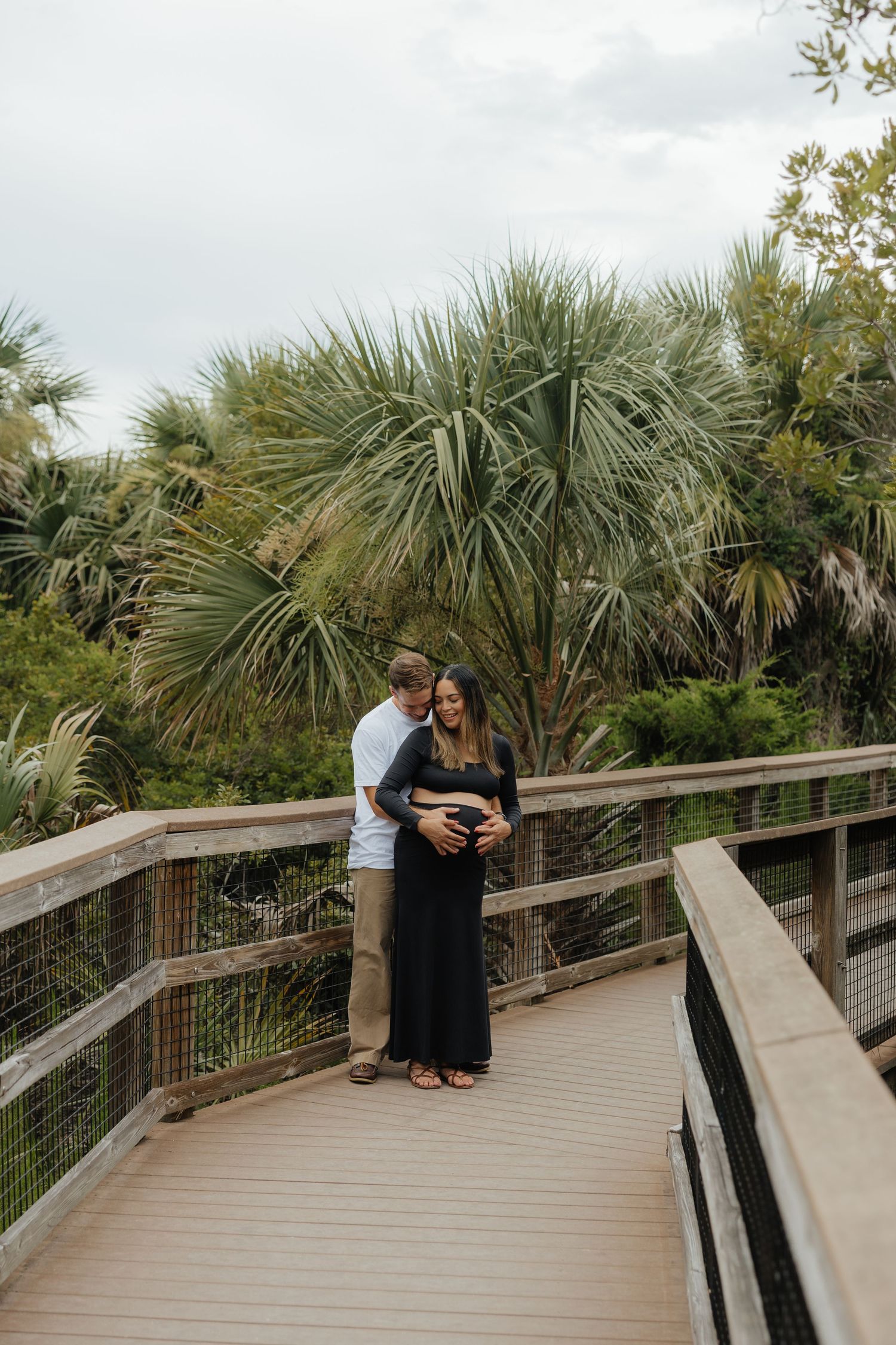 Couple shares intimate moments on a wooden boardwalk surrounded by palm trees in Fort Clinch State Park.