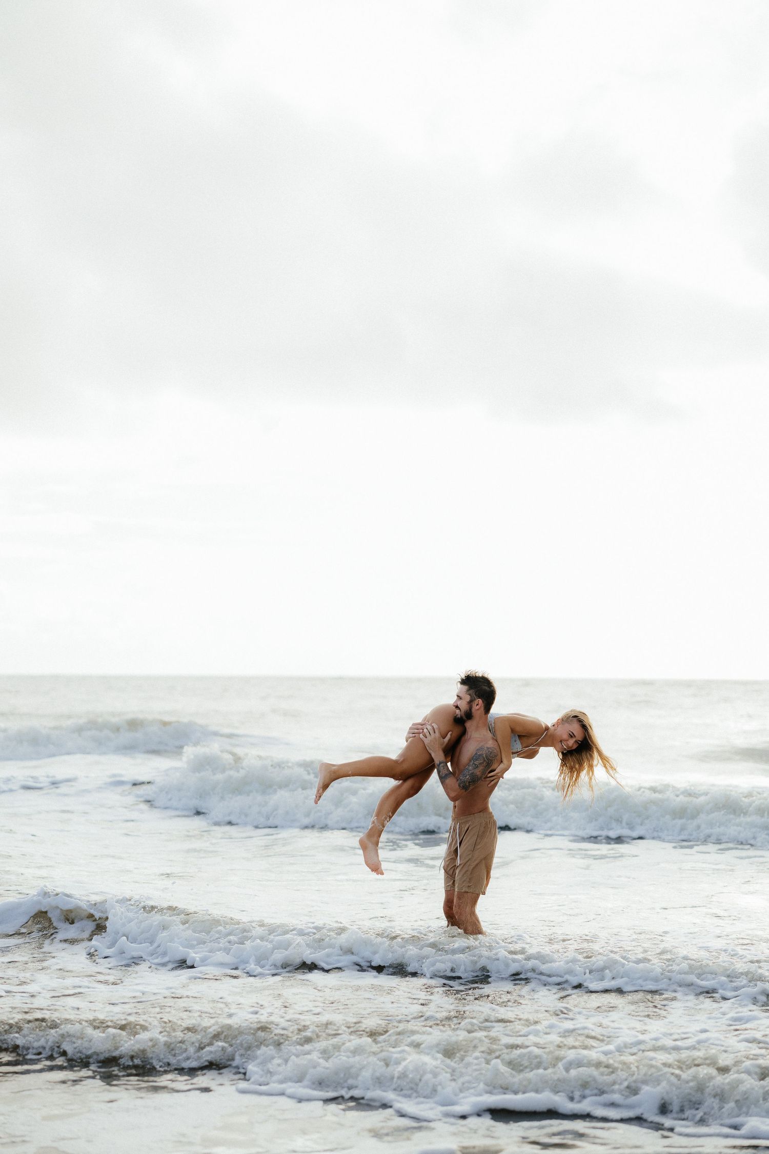 A playful couple spinning around in the shallow ocean waves.