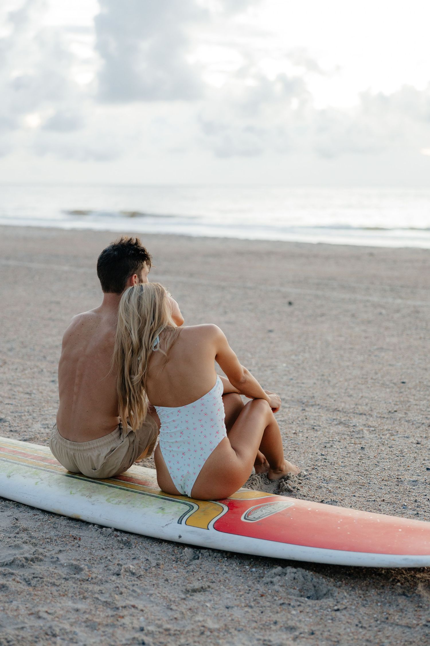 Two people relaxing together on colorful surfboard at the beach.