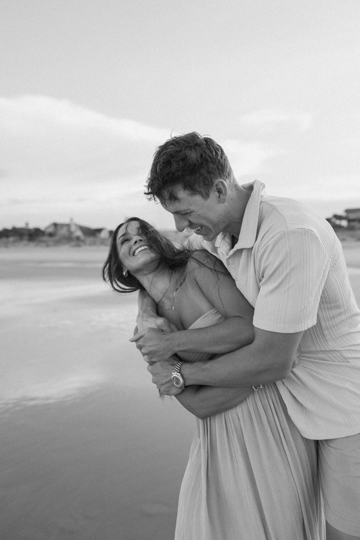 Romantic black and white photo of a couple embracing on a misty beach.
