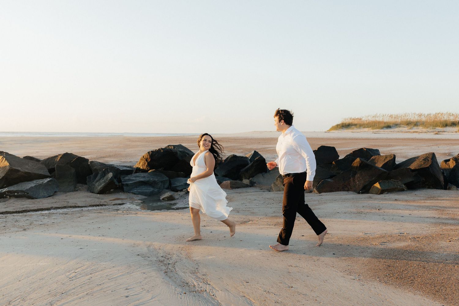 Couple running along beach at sunrise with dark rocks in the background at Fort Clinch State Park.