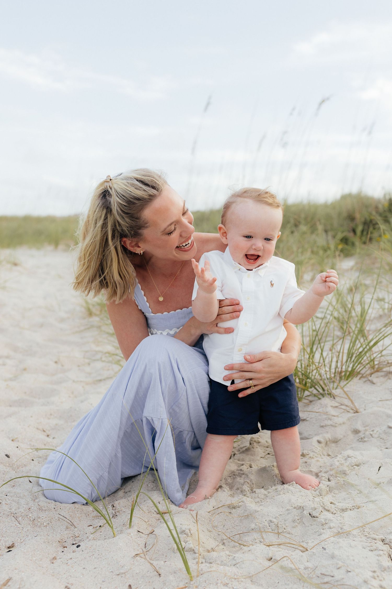 Joyful beach moment between parent and toddler sitting in sand dunes.