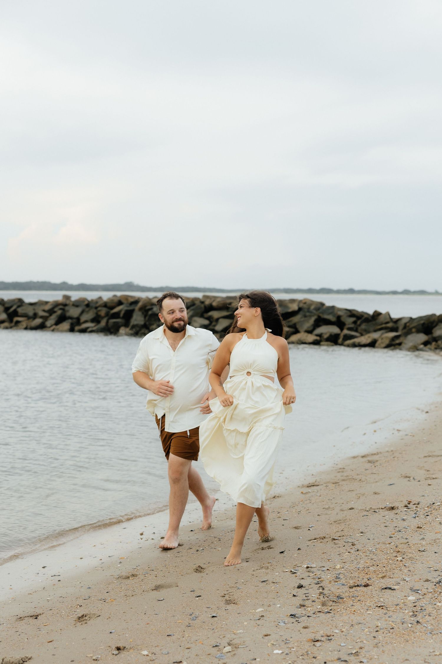 A couple joyfully runs along a rocky beach shoreline at sunset in Fort Clinch State Park.