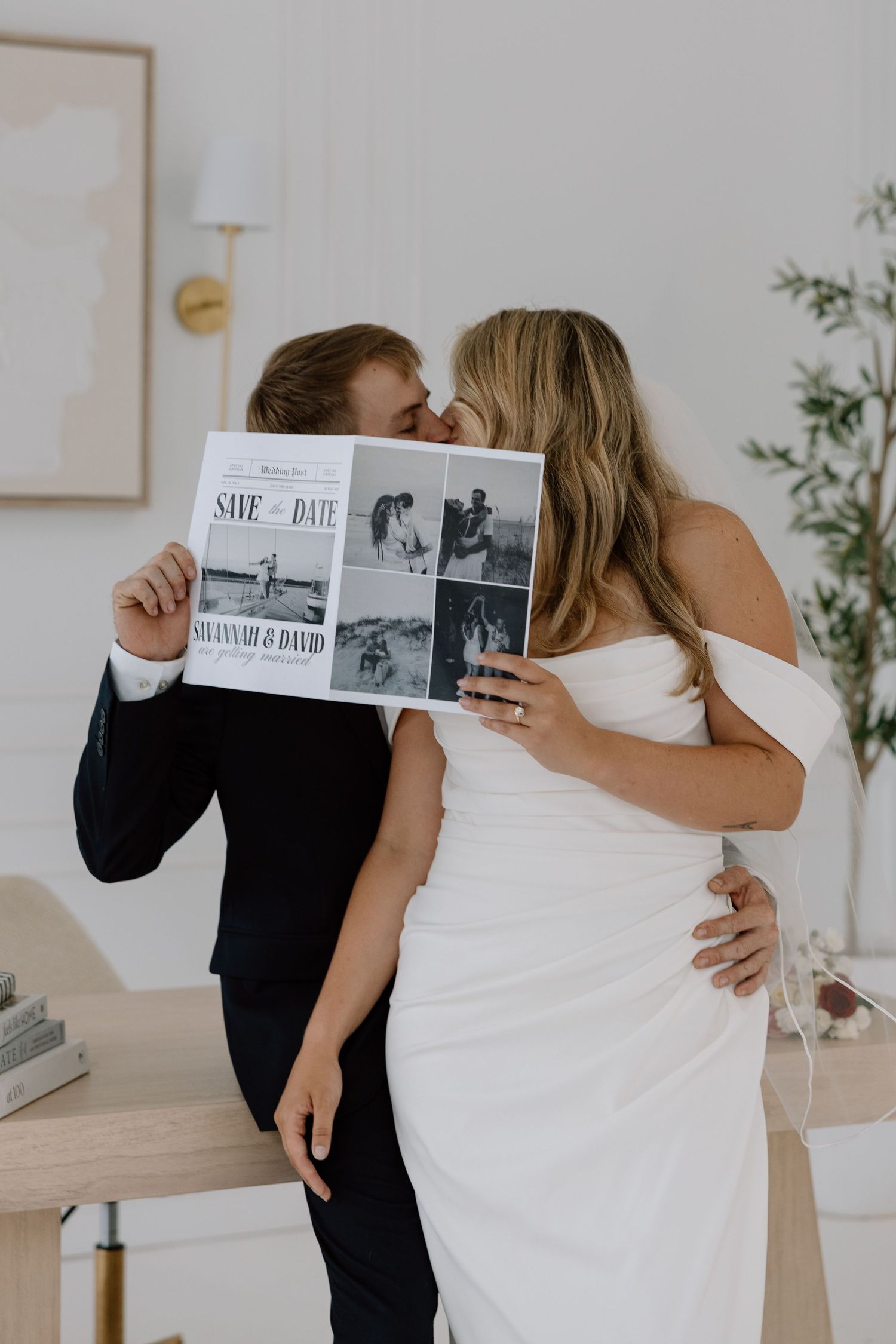 A couple shares an intimate moment while holding their save-the-date announcement.