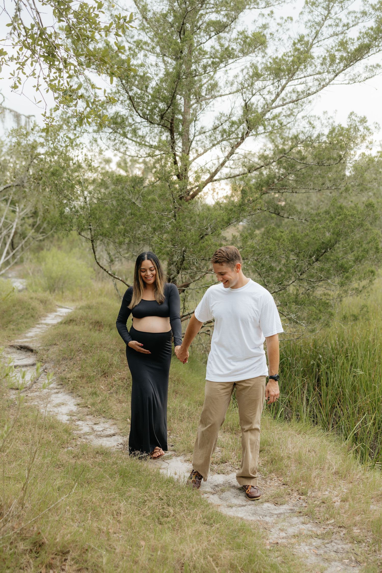 Couple walking together on sandy trail in Fort Clinch State Park through coastal vegetation and grasses on a bright sunny day.