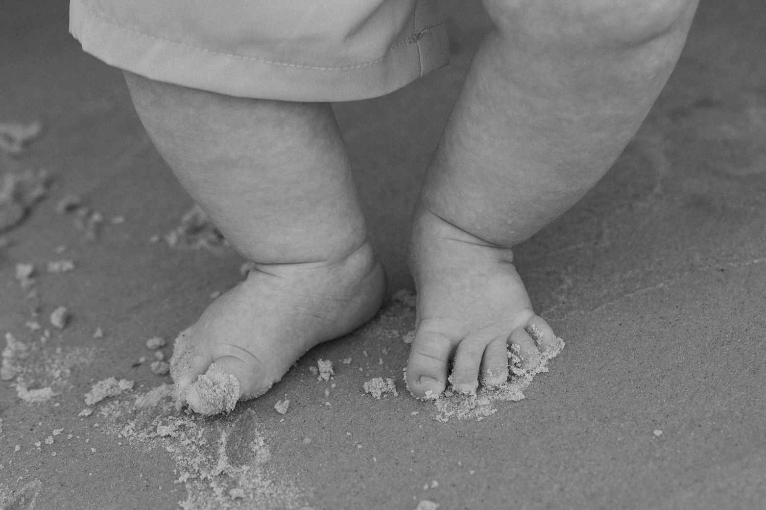 Close-up black and white photo of baby feet in sand on the beach.