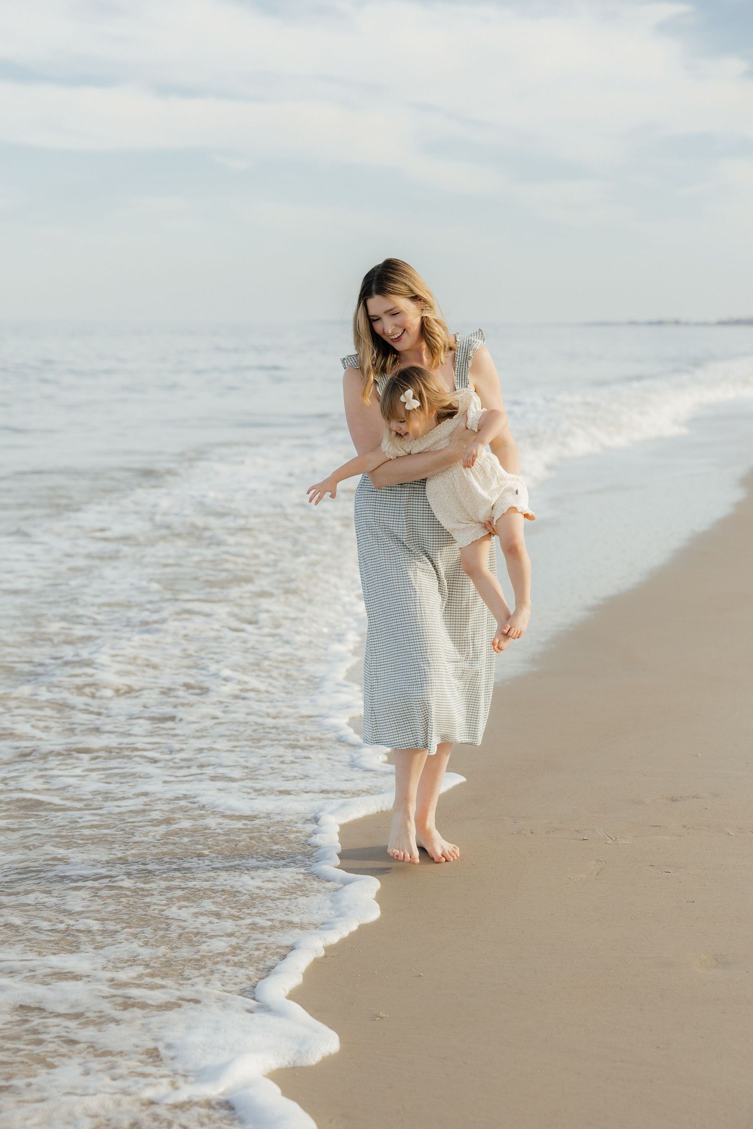 Parent and child playing along ocean shoreline at sunset with waves rolling in.