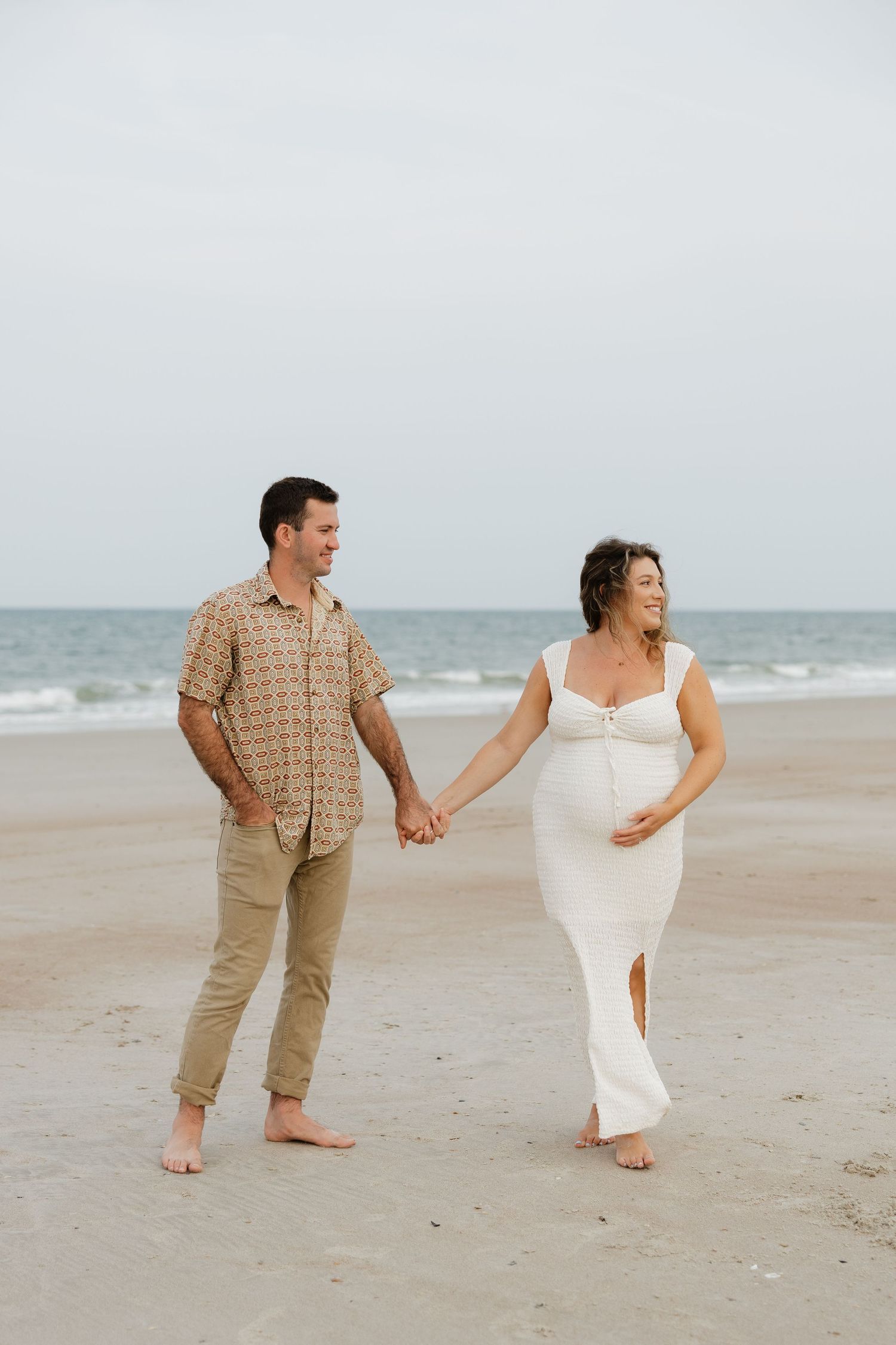 Couple holds hands and runs playfully along the empty beach shoreline.