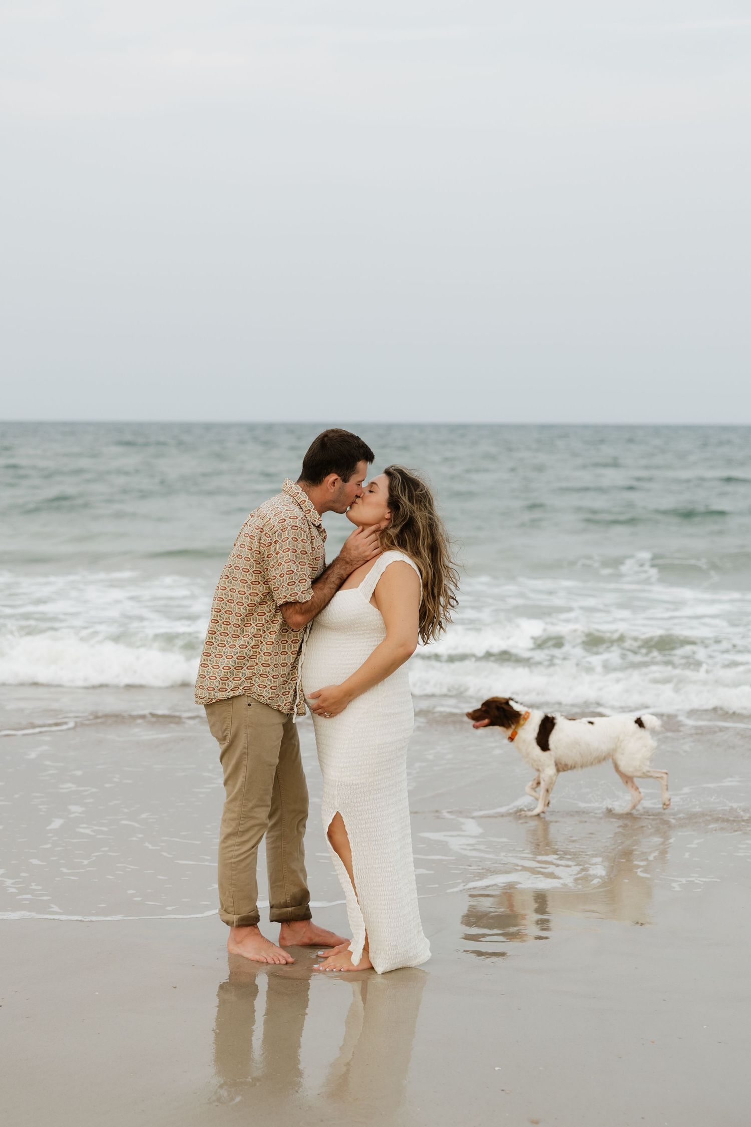 A romantic beach photoshoot features a couple sharing a tender moment by the ocean waves.