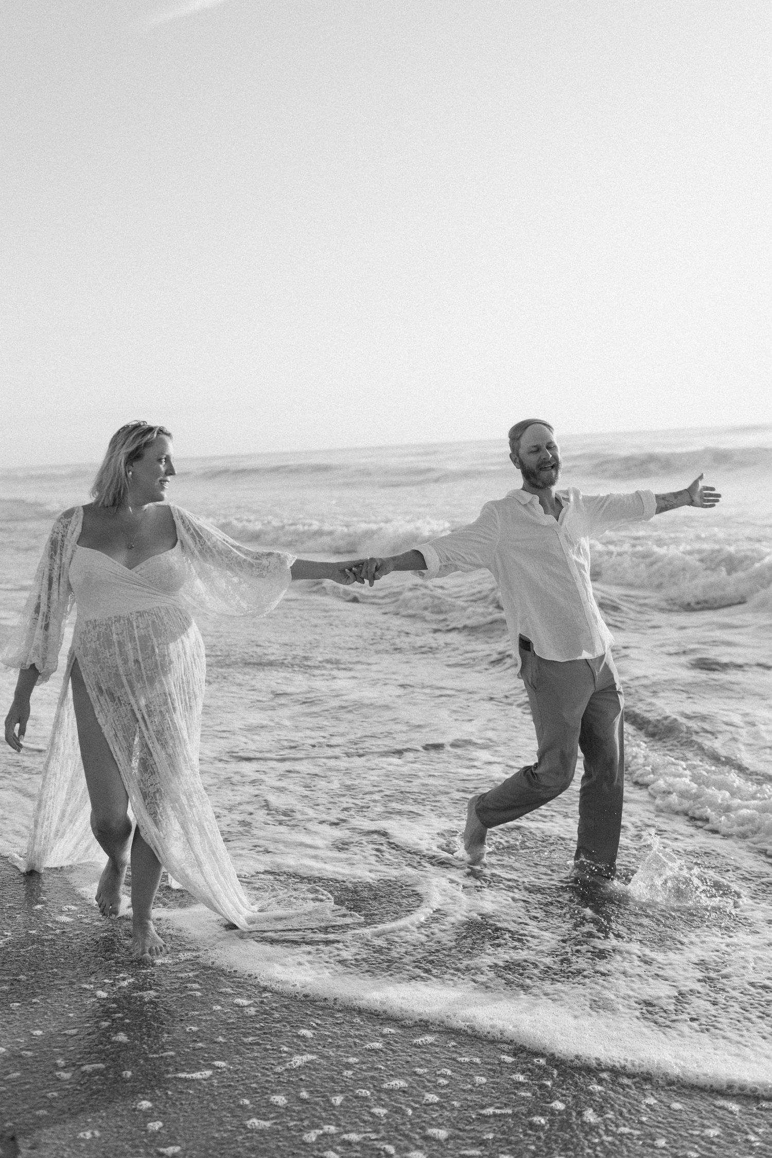 Playful couple splashing in ocean waves during a romantic beach photoshoot.