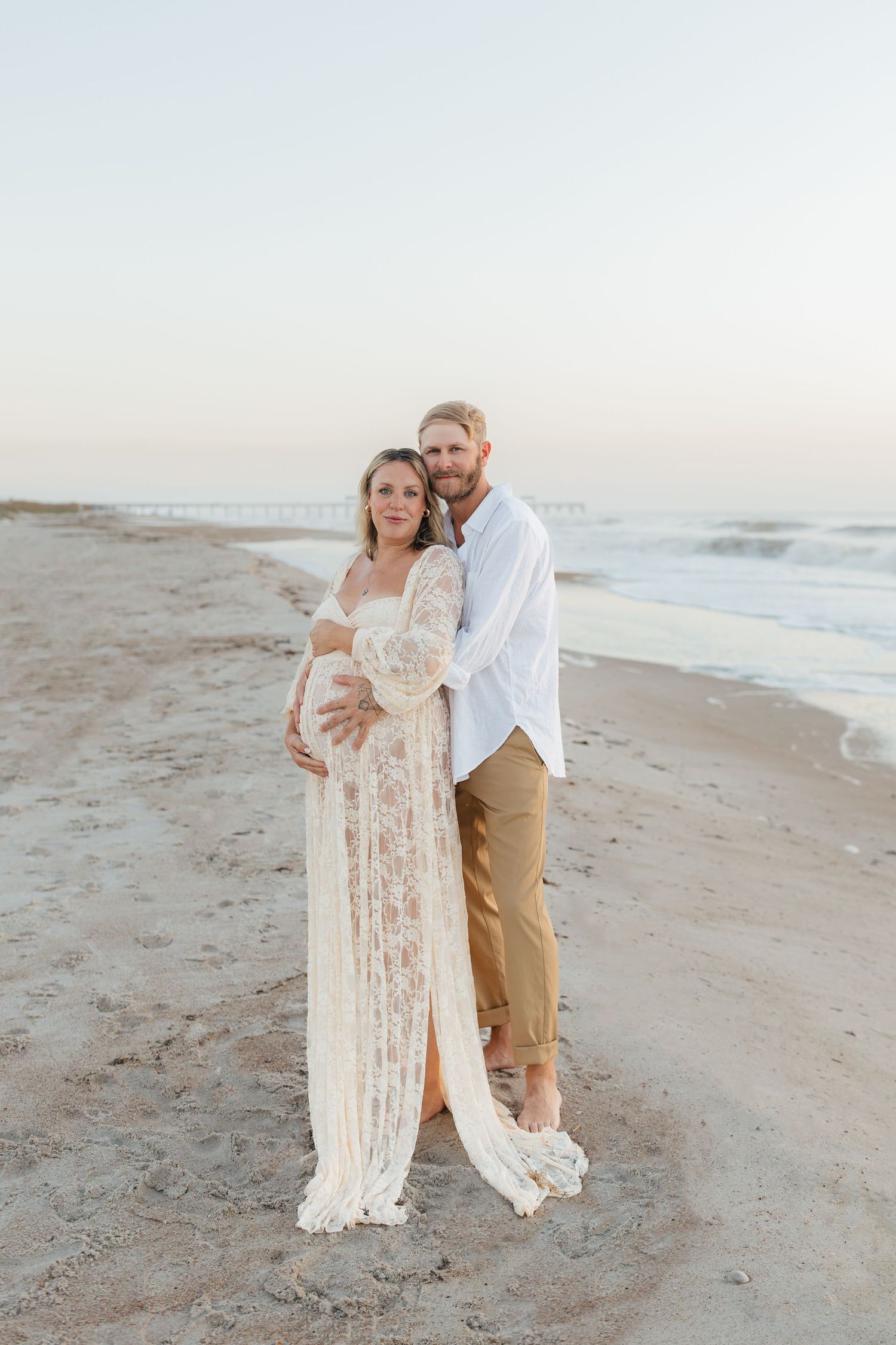 Intimate maternity portrait of couple on beach at dusk.